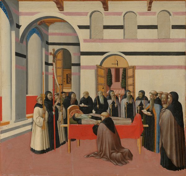 Sixteen men and boys stand around a man lying on a bed, Saint Anthony, in this square painting. A seventeenth mourner kneels on our side of the bed and faces Saint Anthony. Some of the onlookers have their hair cut into rings around their heads, and others’ heads are covered by hoods. They all have pale skin tinged with green, and they wear robes in shades of black, smoky purple, brown, or cream white. A man at the foot of the bed wears a sky-blue robe edged with golden orange down the front as he reads from an open book. Two boys to the left wear white and black and hold tall candles, and a third man, wearing black, holds a cross on a high staff. Others hold candlesticks, walking sticks, books, or stand with hands clasped. Saint Anthony has a long white beard and wears a black hood and muted pink and black robe. One hand rests by his side, and the other rests on his chest. His eyes are closed, and his head is surrounded by a gold and red halo. The bed is draped with a vivid crimson-red cloth. The walls of the room are parchment white striped with mauve pink and black on the upper half. Arched windows and doorways open onto rooms and a courtyard with trees beyond this space. The floor is rose pink.