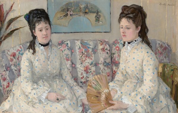 Shown from the lap up, two women with pale skin and dark hair pulled up and back, wearing white dresses with baby-blue polka dots, sit on a couch in this horizontal portrait painting. Both women have straight, dark brows, delicate noses, smooth skin, and their small, rose-pink mouths are closed. Wispy bangs brush their foreheads, and their hair is piled high with long ringlets falling down their backs. Both wear black ribbons like chokers around their necks. Their dresses have high necks with ruffles along the necklines, ruffles at the wrists, and are gathered under the bust. They sit angled in toward each other. The woman on our left has black hair, and she looks down and to our right with dark eyes. She wears a gold ring with a dark, oval stone on one hand resting in her lap. The other woman has chestnut-brown hair and looks down and off to our left with ice-blue eyes. She holds an open fan in her hands in her lap. The fabric on the couch has vertical white and lilac-purple stripes, and is overlaid with a pattern of pink flowers and green leaves. A framed picture hanging on the bone-white wall behind the women shows an arched painting against a sky-blue background. A few spiky leaves from a houseplant are cut off by the left edge of the painting. The portrait is loosely painted throughout, especially in the couch and background. The artist signed the painting in the upper right corner, “Berthe Morisot.”