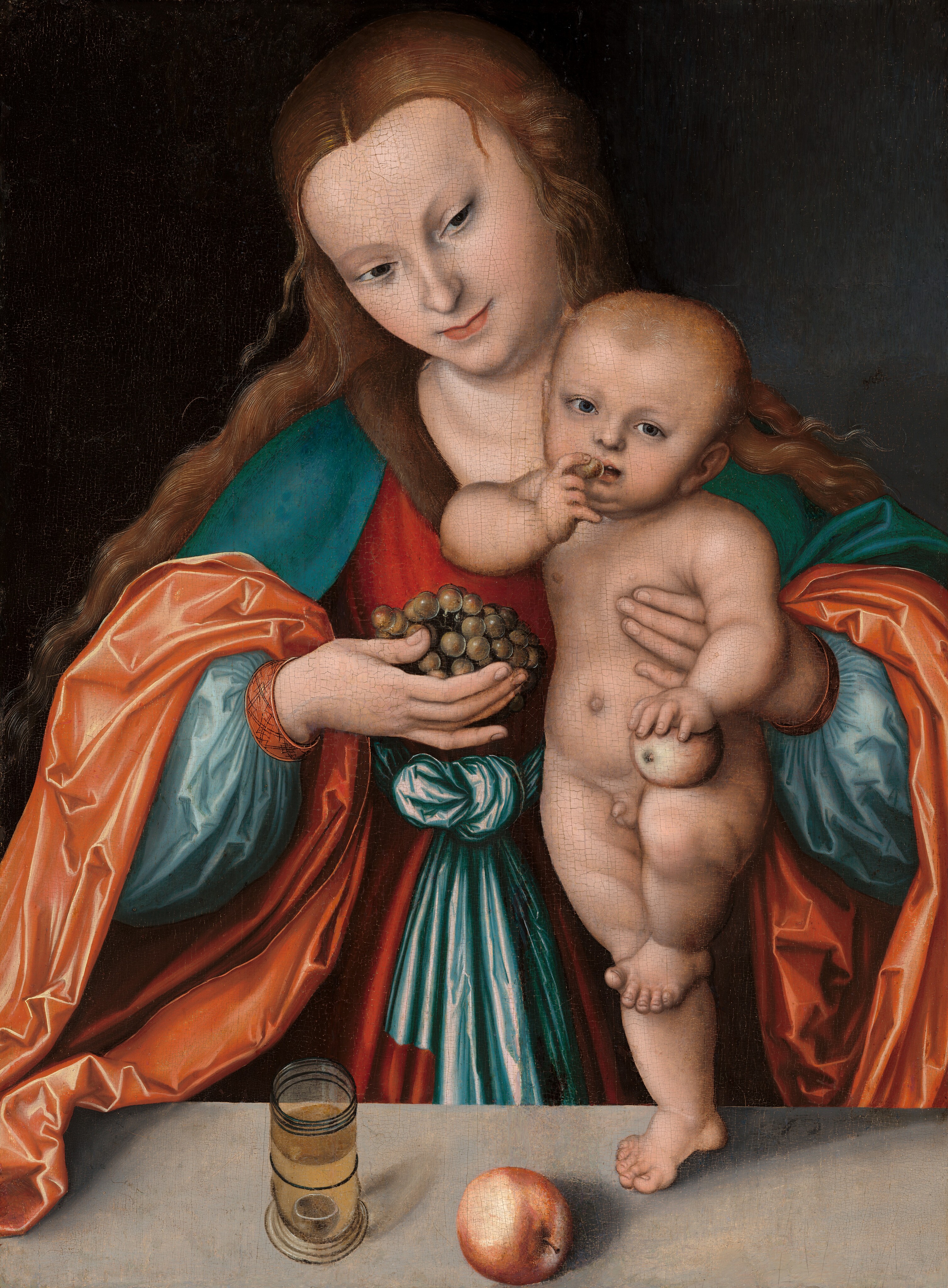 This painting shows the upper half of a woman and a standing infant. The woman stands behind a table while the infant stands on one leg on top of it. She holds the child steady with one arm. The woman has fair skin, long brown hair, and a serene expression as she looks down at the child. She wears a colorful dress with wide sleeves in shades of bright red, teal, and orange. With her other hand, she holds a bunch of green grapes towards the child. The unclothed infant has light skin and light hair, and it stands comfortably with one foot on the ground and the other resting on its knee, holding an apple in one hand and lifting a grape to its mouth in the other. The background is dark, and on the gray table at the bottom of the painting there is a glass of yellow liquid and another apple.