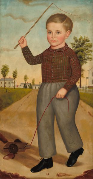 The image shows a young boy standing on a dirt path, holding strings attached to a wooden toy with wheels. He is raising his left hand with a stick. The boy has short, neat light brown hair, fair skin, rosy cheeks, and bright eyes. He wears a red and green checkered shirt, gray trousers, and black shoes. In the background, there are white houses with red chimneys, trees, a sky with clouds, and a picket fence.