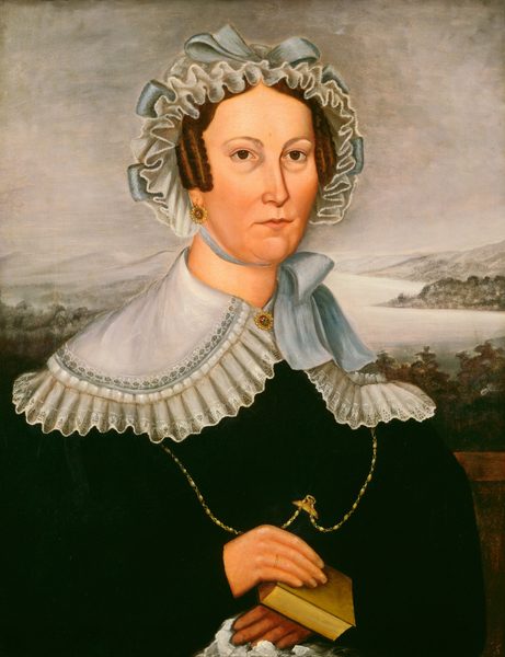The image shows a woman with the upper torso visible. She is facing forward holding a closed book with her hands together. The woman has fair skin, dark eyes, thin eyebrows, and brown curly hair framing her face. She wears a lace cap and a dark dress with a white lace collar. She has gold earrings with red jewels, and a gold chain with a key or locket. In the background, there is a landscape with trees and water under a cloudy sky.
