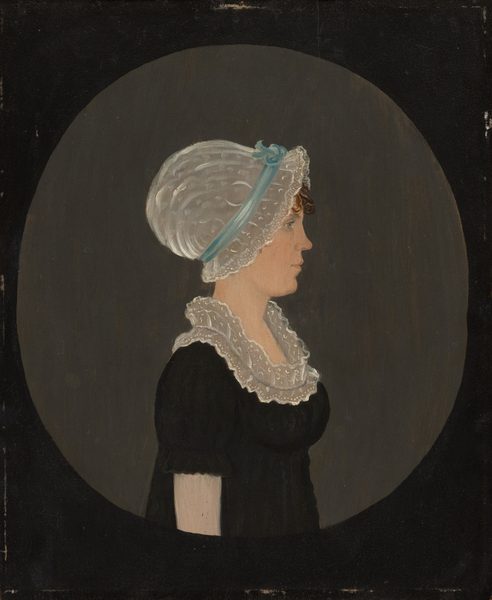 The image shows a woman in profile. She is seated with her torso turned slightly to the left. Her facial features include a straight nose, closed lips, and she wears a lace cap with a blue ribbon. Some brown curls peek out from under the cap. She wears a dark dress with short sleeves and a white lace collar. There is no visible jewelry or objects in her hands. The background is a solid dark circle against a neutral backdrop.