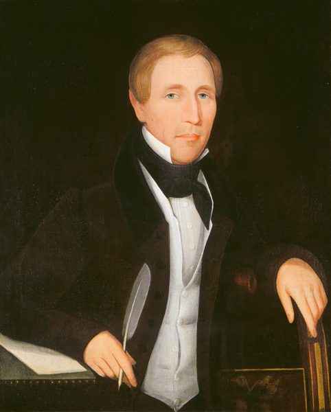 The image depicts the upper half of a seated man with fair complexion, blue eyes, light brown hair styled neatly, and a composed expression. He is dressed in a dark suit with a high-collared white shirt and a black cravat. The man's right arm rests on the chair's arm, while his left hand holds a quill pen. In the background, there is a stack of papers.