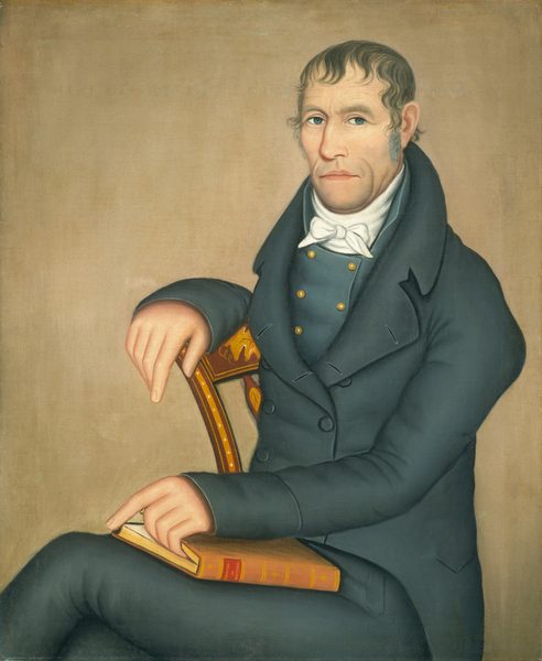 The image shows a man in a side-profile position. He has light blue eyes, a long nose, thin lips, and dark brown, wavy hair with sideburns. He wears a dark coat, a white high-collared shirt, and a white cravat. The man rests his arm on the back of a wooden chair and holds a closed book. The background is a neutral-toned canvas.