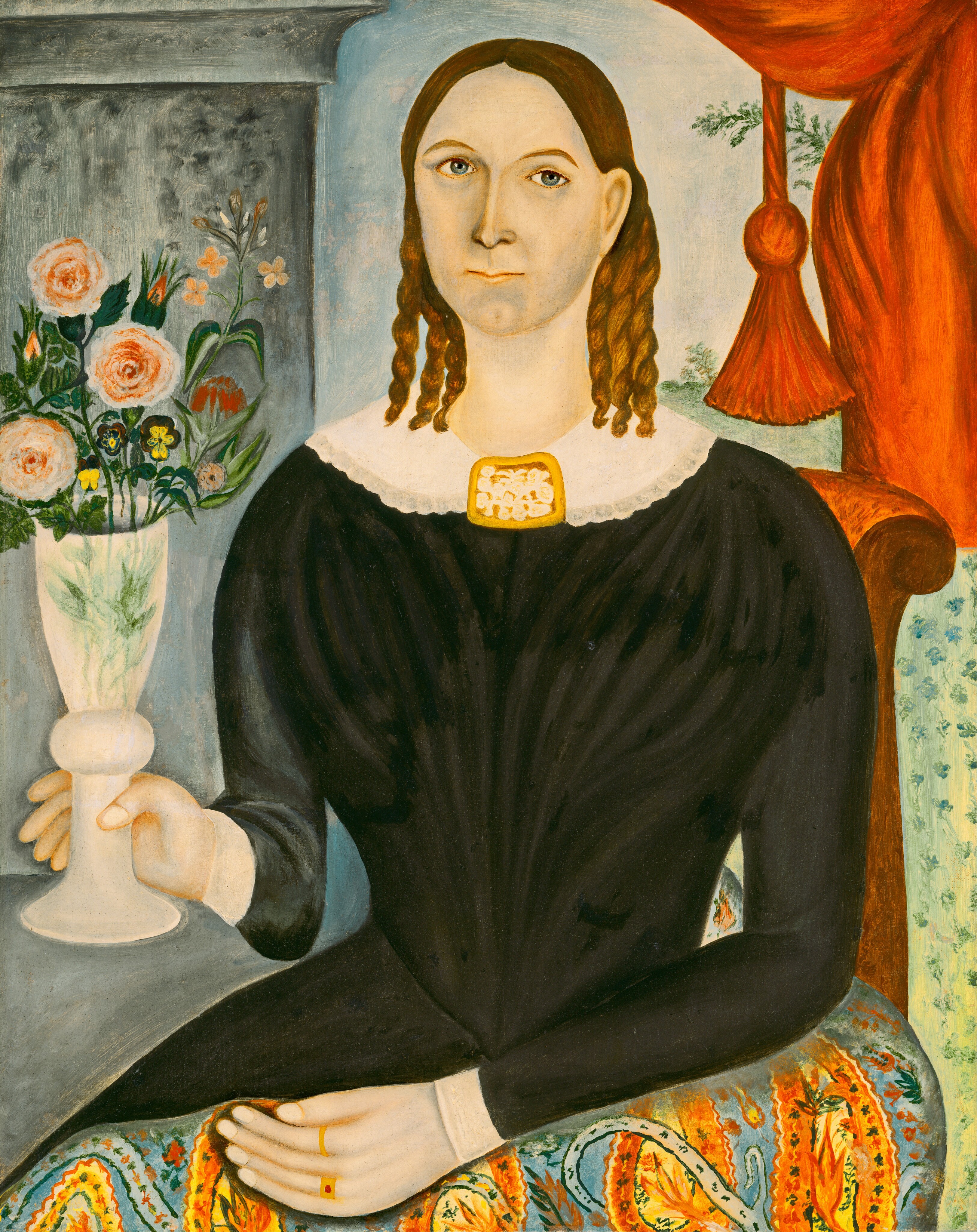 The image depicts a painted portrait of a woman from the waist up. She is seated and facing directly towards the viewer with her right arm resting on a surface, holding a white vase containing pink and orange flowers. Her facial features include large, light-colored eyes, a straight nose, and a closed mouth, with tightly curled, brown hair falling over her shoulders. She is wearing a dark, long-sleeved dress with a white lace collar and a brooch. On her lap, there is a colorful patterned fabric with hints of yellow, blue, and orange. She wears a ring on her right hand. The background consists of a wall with an ornate, red curtain draped to her right and a detailed blue pattern behind her.
