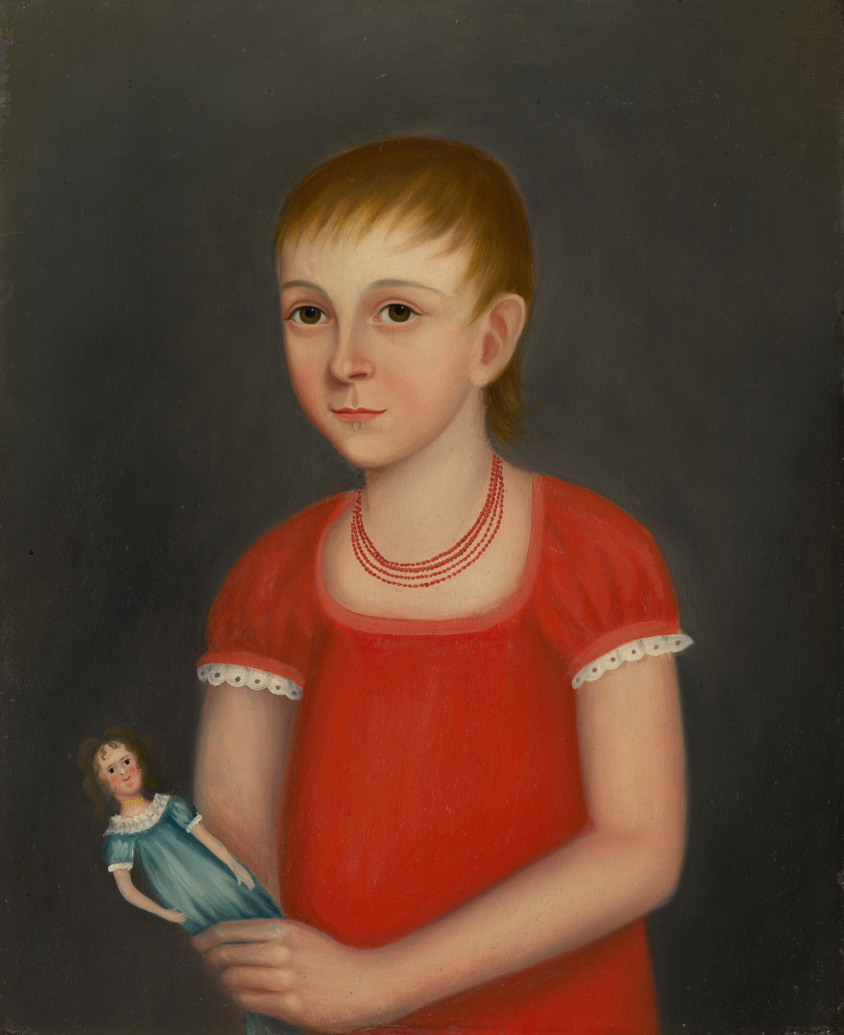 The image shows the upper half of a young individual facing slightly left. The individual has short light brown hair, dark eyes, a small nose, and closed mouth. They wear a red dress with white lace trim, and a red beaded necklace. They hold a small dark-haired doll in a blue gown with white lace. The background is dark.