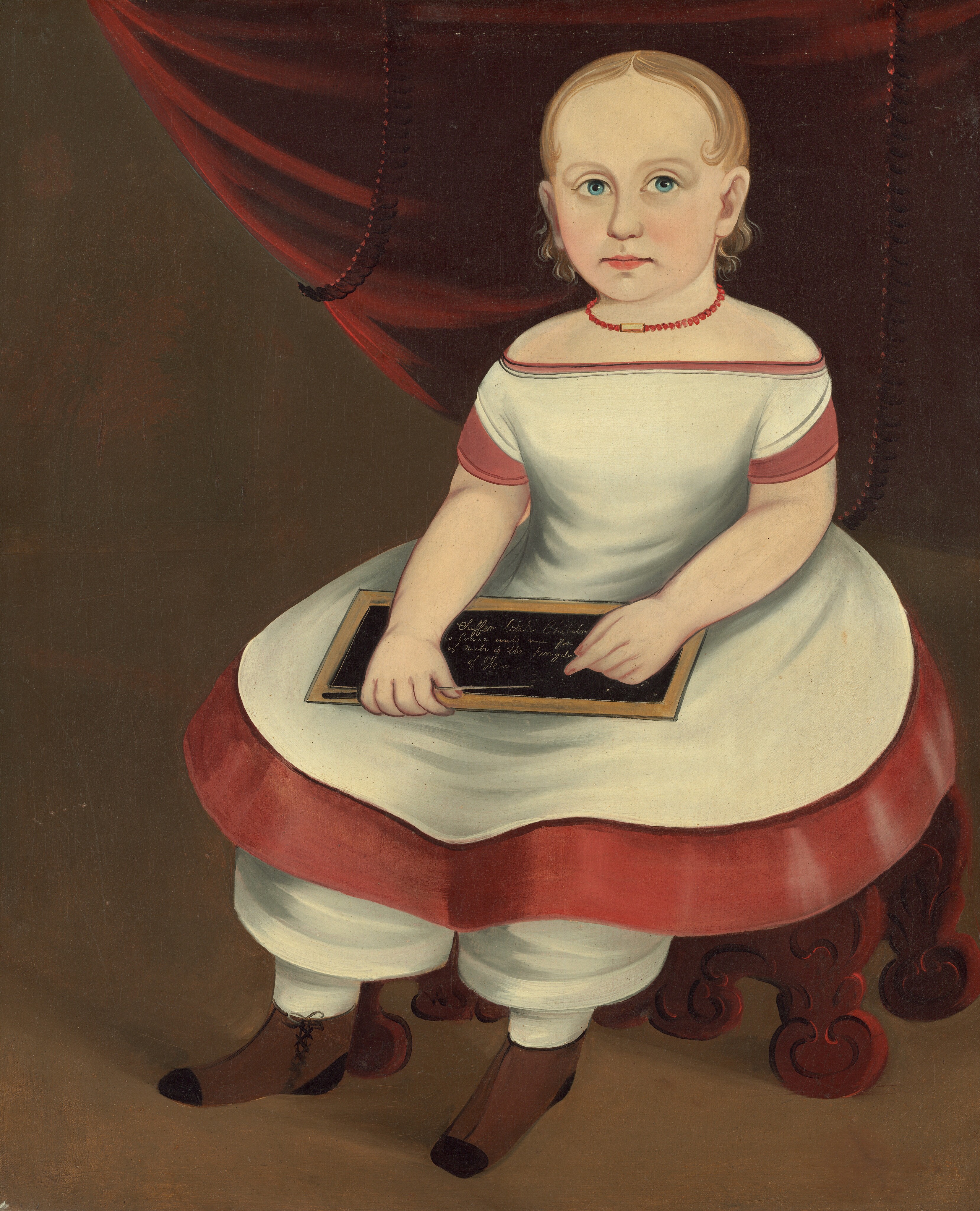 The image depicts a young child seated on a carved wooden chair, facing forward with legs hanging over the edge. The child holds a small chalkboard with writing on it and has light blonde hair, big blue eyes, wearing a white dress with red trim, white pants, and brown lace-up boots. There is a red necklace around their neck and a dark brown background with a red curtain partly visible.