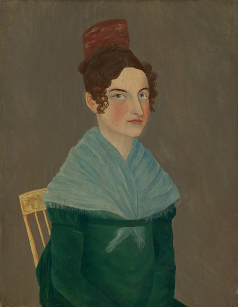 The image depicts a person sitting on a wooden chair with a decorative backrest. The individual is facing slightly to the right, making eye contact with the viewer. They have fair skin, blue eyes, reddish lips, and dark curly hair styled with a wave, partially covered by a brown fez-like hat. The person is wearing a dark green garment underneath a light blue fringed shawl. The background is a plain, muted brown color.