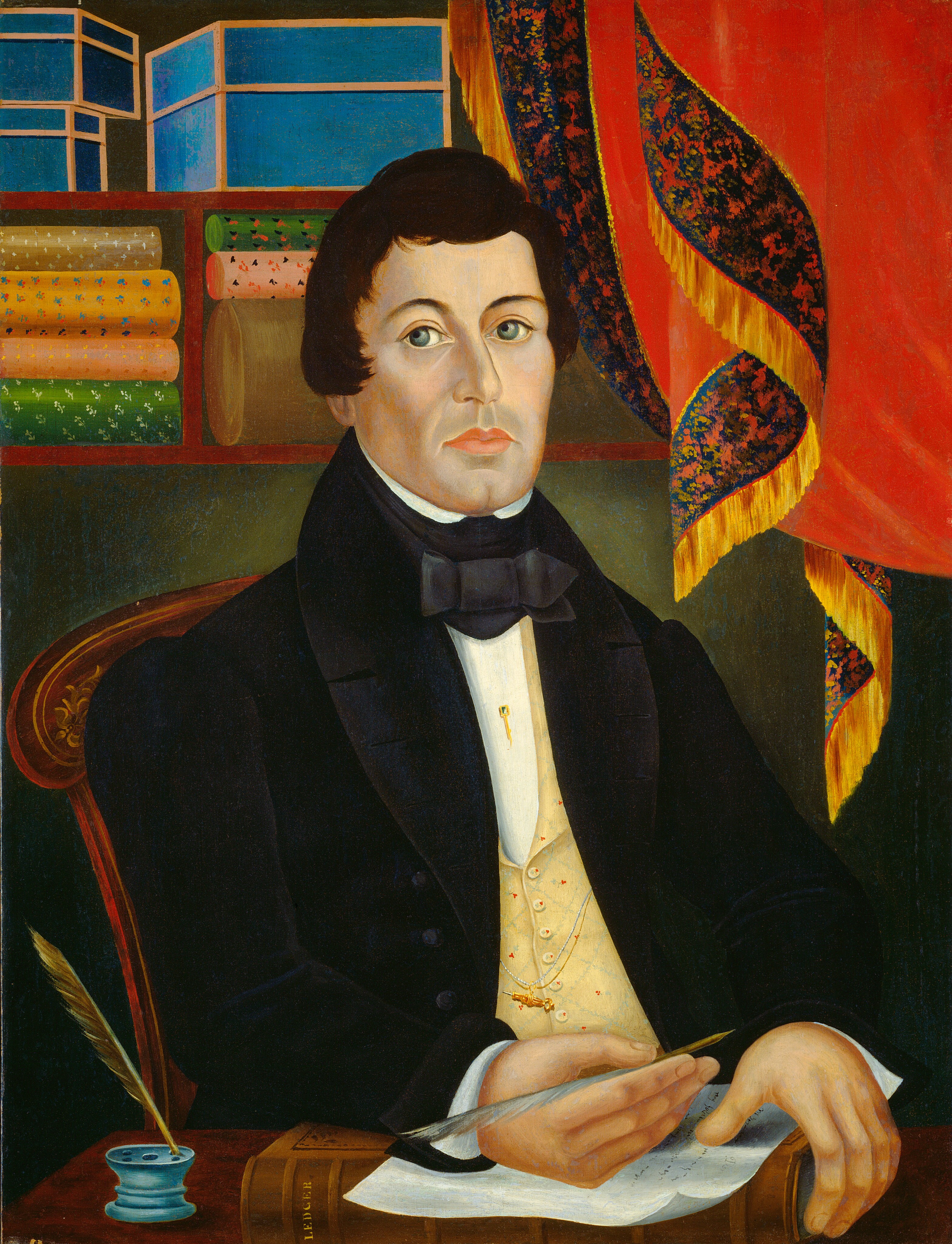 This painting shows the upper body of a man seated at a table. He is holding a quill over a sheet of paper, and his body is turned slightly to the right as he looks out at us. He has a fair complexion, large green eyes, a straight nose, and a neutral expression. He has dark, wavy hair, and is dressed in a formal black jacket with a white shirt underneath, a black bow tie, and a yellow waistcoat adorned with a gold-colored chain and a pin. On the brown table he sits behind, there is an ink pot with another quill in it, and a thick brown book partially covered by the paper he writes on. Behind his head are rolls of patterned fabric on shelves, along with several blue boxes. The walls are a dark green color, and on the right is a bright red curtain with a black pattern on the gold-fringed edges.
