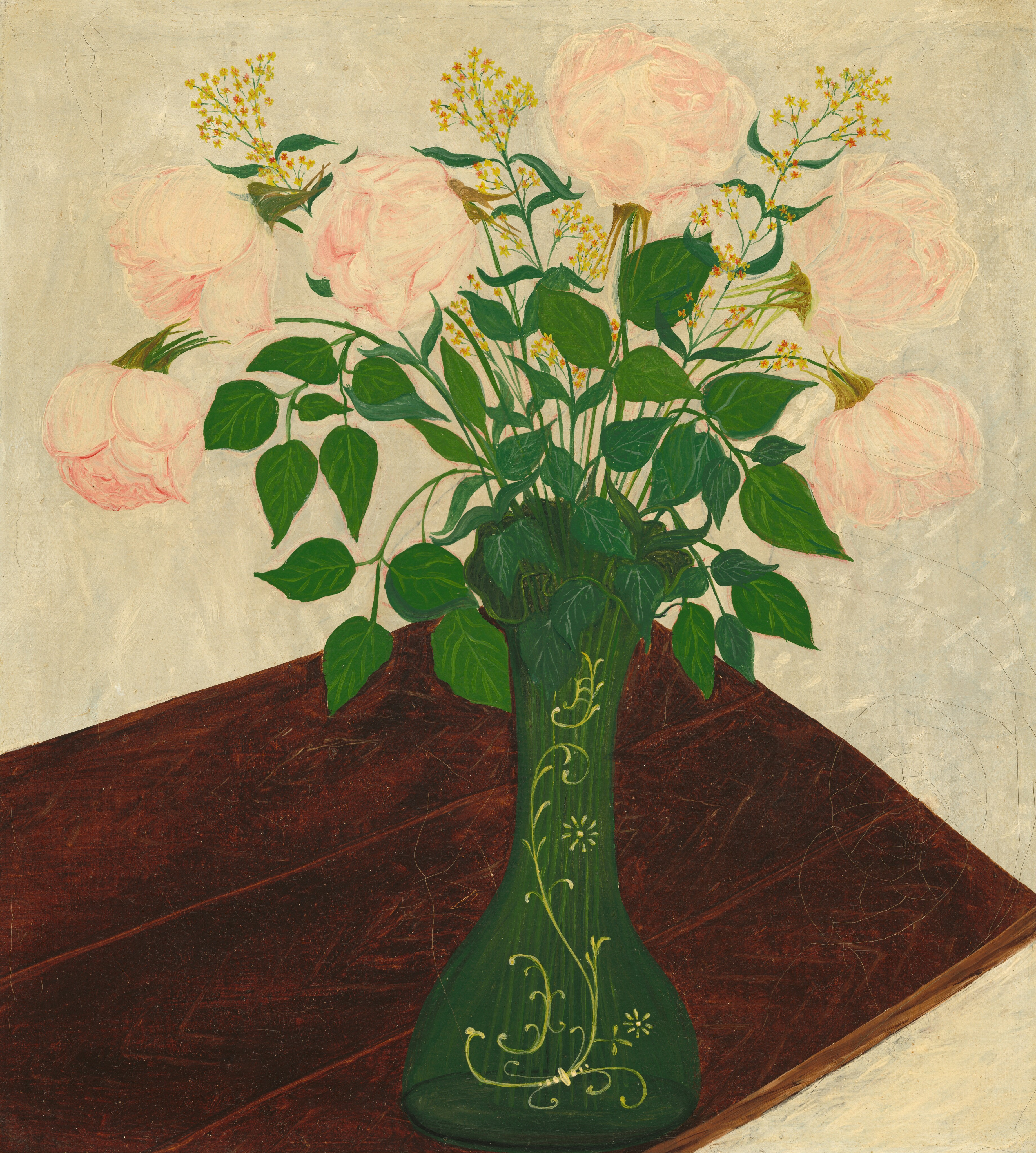 In this painting, a bouquet of large, pale pink roses fills a green vase decorated with yellow floral patterns, which is resting on a wooden table with a rich, dark brown surface. Flowers extend outward from the center to fill much of the upper portion of the image, while the wooden surface stretches diagonally from the bottom left corner to the center. The pink roses are surrounded by green leaves and smaller groups of yellow flowers. The wall behind the flowers is a pale gray color.