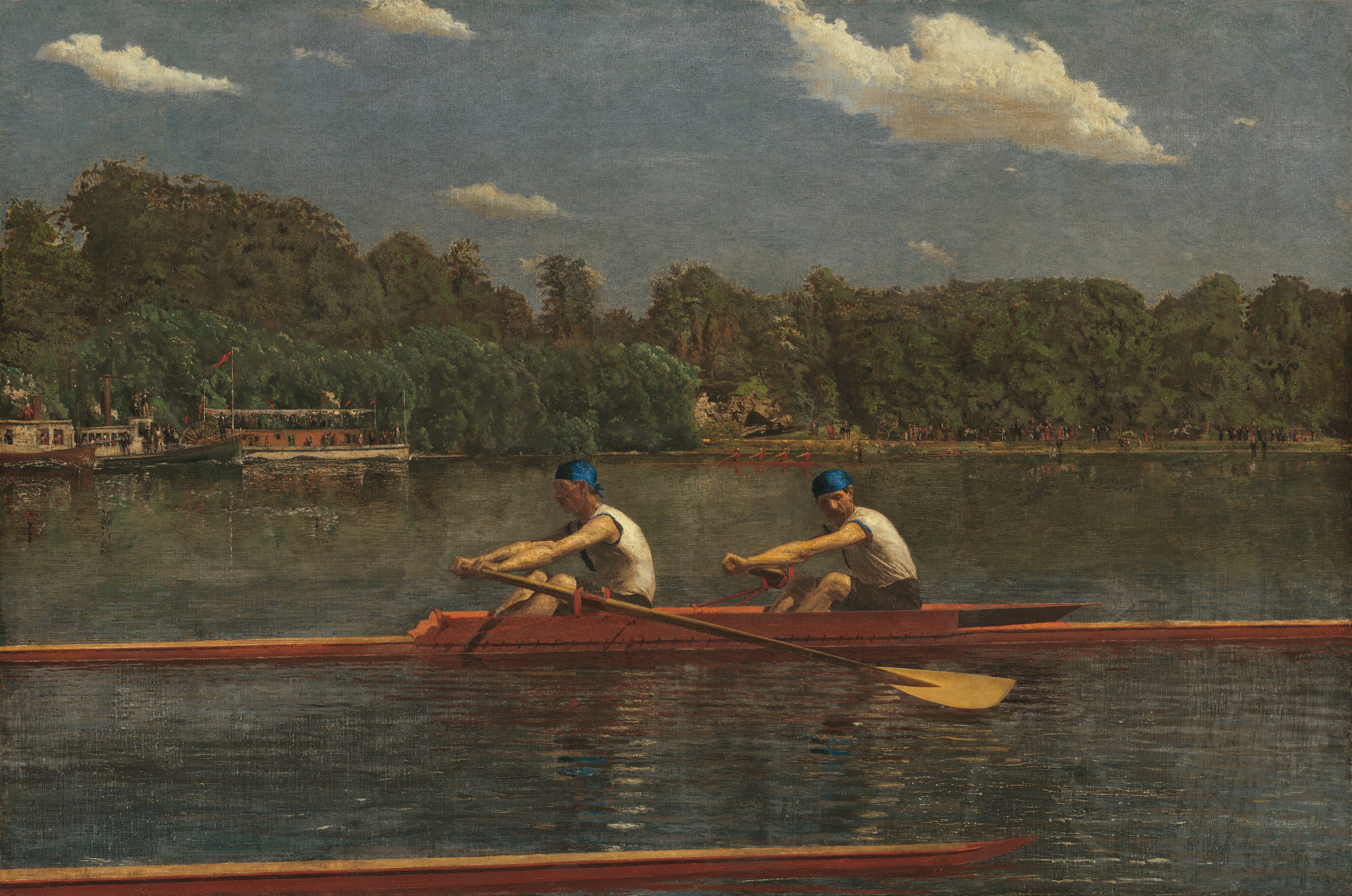 Two men with pale skin, wearing white sleeveless shirts and royal-blue caps, row in unison in a long, narrow boat on a placid blue river in this horizontal landscape painting. The low, honey-colored wooden boat extends off both sides of the canvas. Both men face our left as they row to our right. The man in front looks ahead of him, beyond the stern of the boat, and the man to our right, closer to the bow, tucks his chin down to look past his shoulder. Their bare, muscled arms are extended straight as the two oars sweep back. The tip of another boat runs close and parallel to the bottom edge of the composition, spanning the left three-quarters of the painting. The opposite riverbank is lined with a dense forest of pine-green trees. People crowd along the decks of a steamboat and a paddleboat near the riverbank to our left. Another narrow skuller, rowed by four people wearing ruby-red shirts, cuts through the water at the back center of the river. The riverbank beyond is lined with people, painted with strokes of black and white, and minuscule touches of red. The horizon comes halfway up the composition. Cream-white clouds float across a muted, topaz-blue sky above the trees.