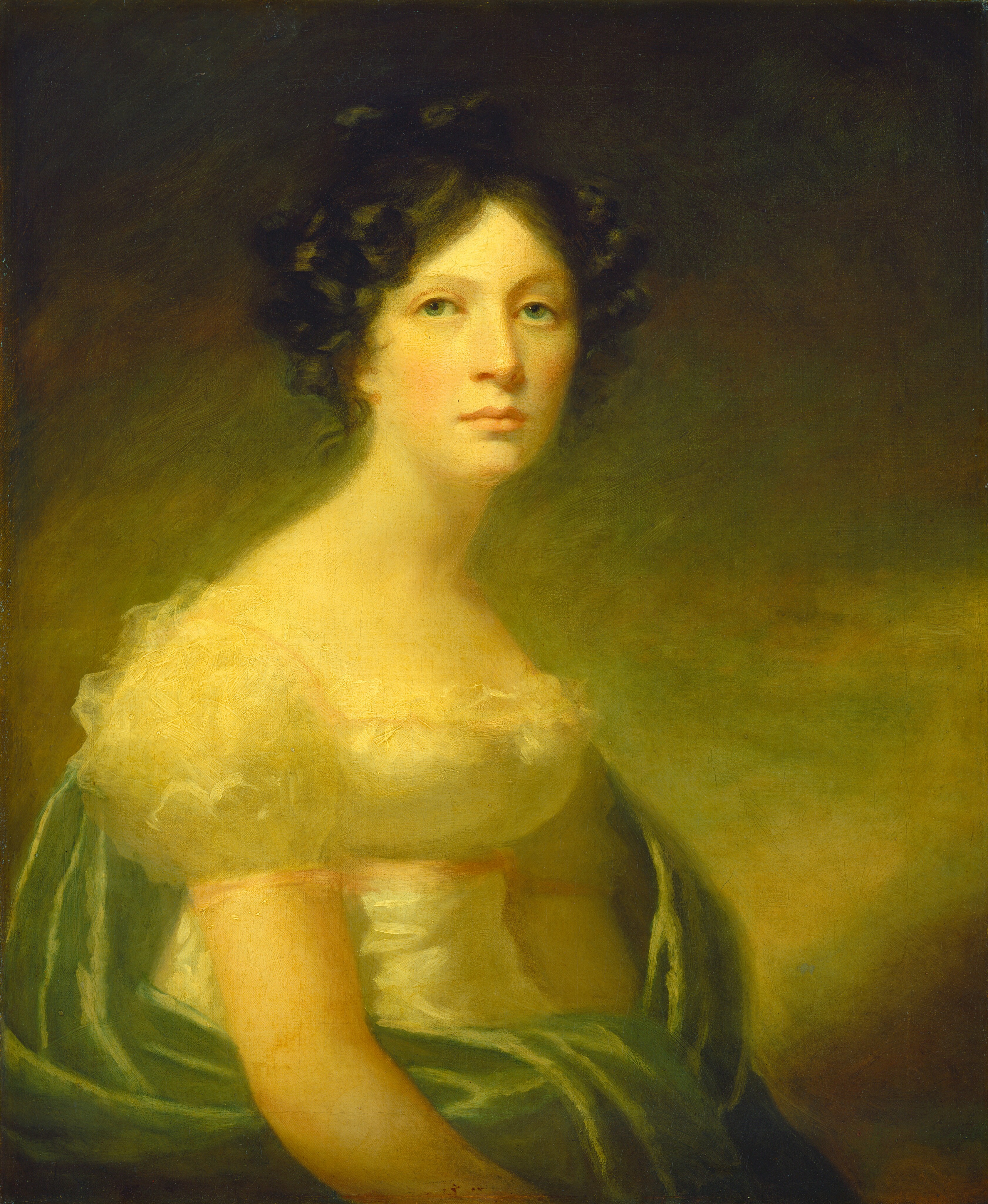 The image shows a portrait of a person from the waist up. The individual is facing slightly to the right with their head turned towards the viewer. The person has fair skin, green eyes, dark curly hair, and is wearing a white gown with lace trims on the shoulders and neckline. In addition, there is a green draped fabric that complements the attire. The background is a warm-toned gradient.