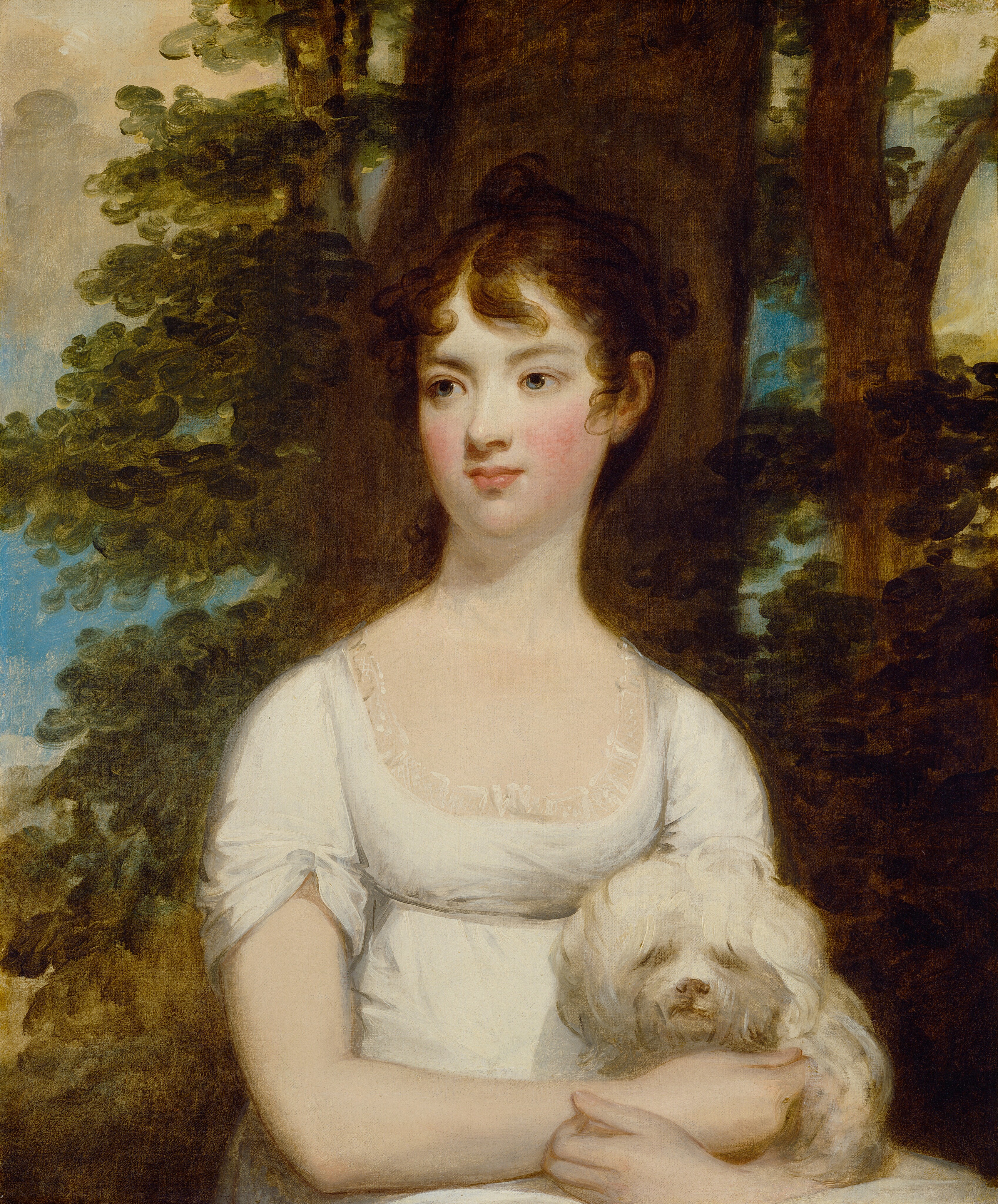 This painting depicts a woman seated with a small white dog in her lap, her head turned slightly to the left. She has pale skin, rosy cheeks, faint eyebrows, light-colored eyes, and small pink lips slightly curved up at the edges. Her curly, dark-brown hair is styled up, and she is wearing a short-sleeved white dress with lace details around the neck. The background shows brown trees with dark green leaves against a blue sky with gray clouds.