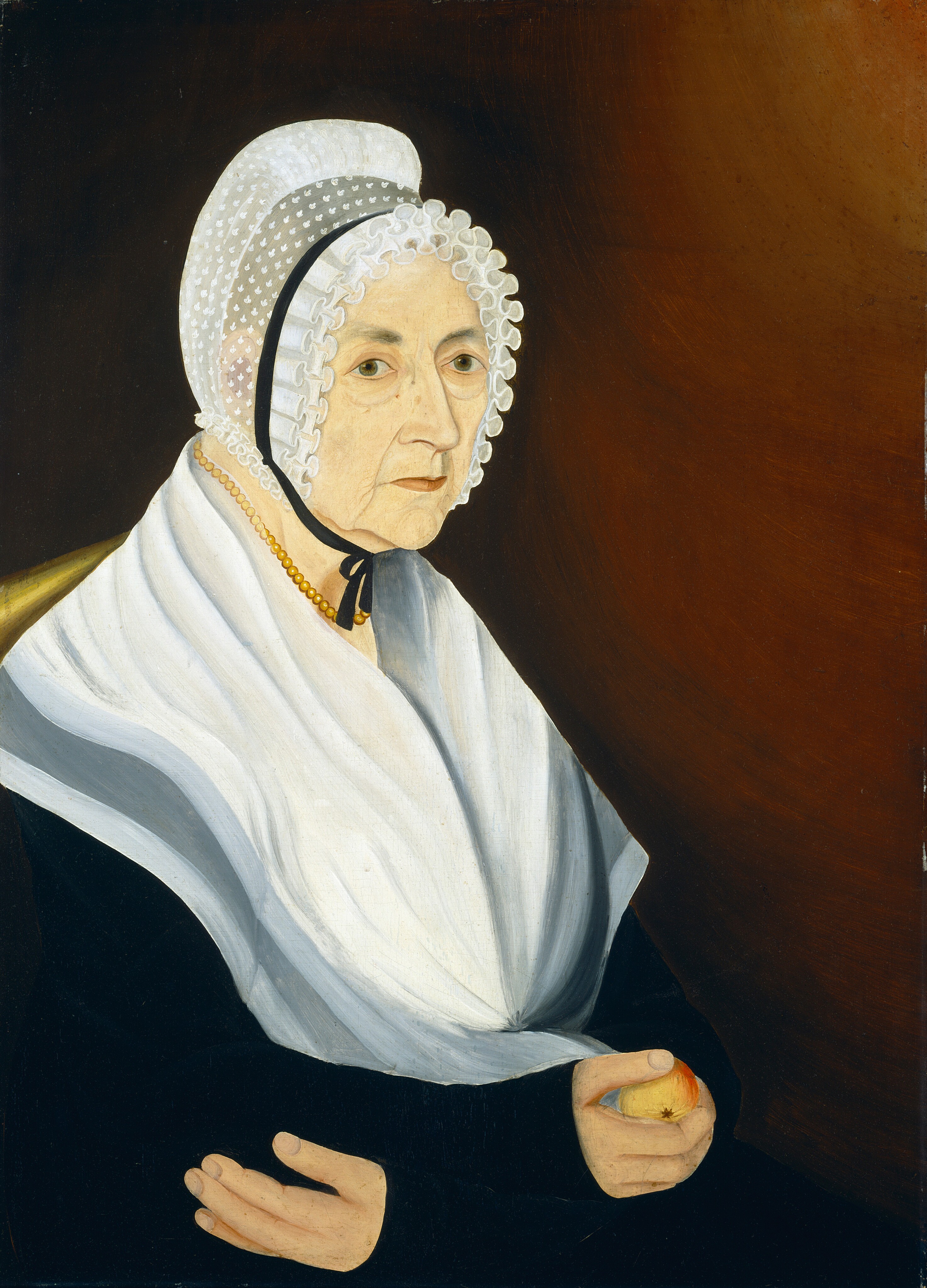 The image shows the upper half of an elderly woman seated in a three-quarter view, facing slightly to her left. Her facial features consist of soft and aged skin with wrinkles. Her eyes are pale blue, with thin eyebrows. She wears a white lace bonnet tied under her chin with a black ribbon. A dark garment and a white shawl are draped over her shoulders. She wears a strand of amber-colored beads around her neck and holds a small apple in her right hand. The background is a warm, brownish color.