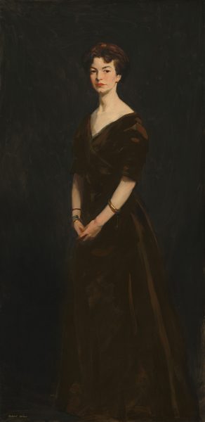 This painting is a full-body portrait of a woman. She is standing in an upright position with her hands clasped together in front of her body. Her body is faced slightly to the left, but her face is turned to us. Her face is serious, with pale skin, dark, arched eyebrows, a cleft chin, and red lips in a neutral expression. She has short, dark, softly curled hair. She wears a dark dress with wide shoulders, a V-shaped neckline, and elbow-length sleeves, accessorized with gold bangles on her wrists. The background is a dark, almost black, monochromatic backdrop that blends in with the bottom of her skirt.