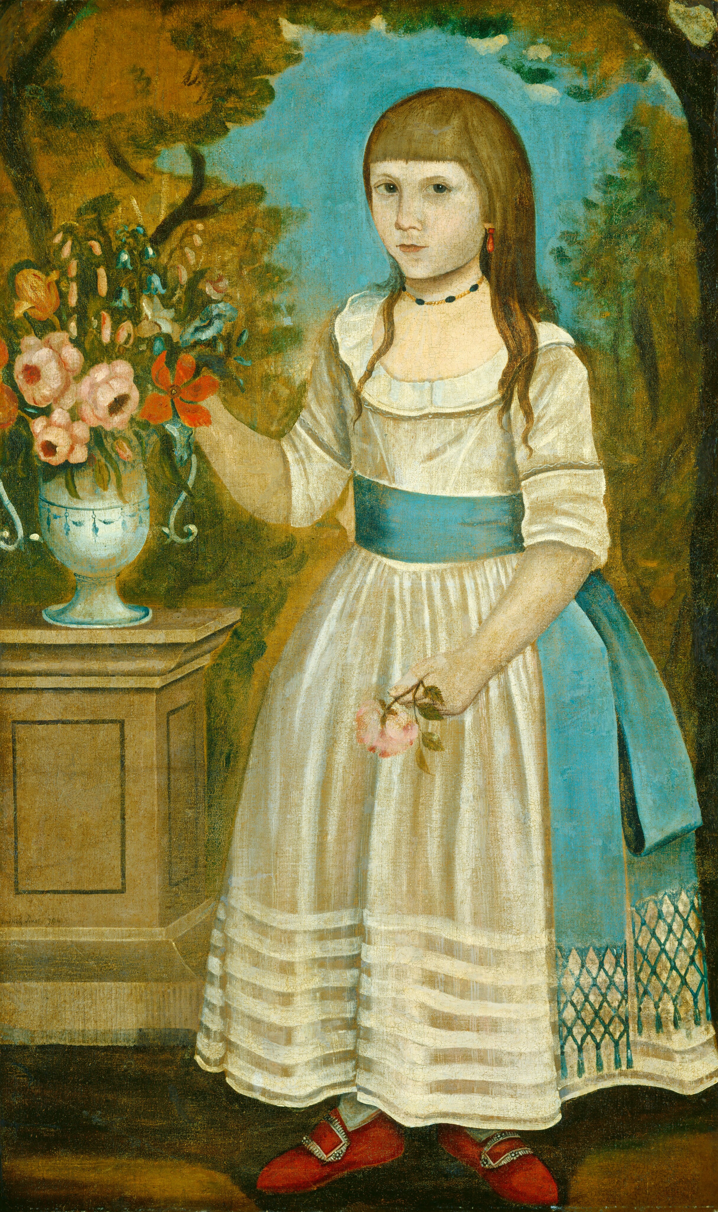 The image features a young girl standing facing the viewer. She holds a red flower in her right hand and a small bunch of pink flowers in her left hand. She has delicate features, light skin, long brown hair with bangs, and wears a white dress with blue sash. She wears red shoes, a black bead necklace, and an orange earring. Next to her is a pedestal with a vase of colorful flowers. The background shows a blue sky and trees.