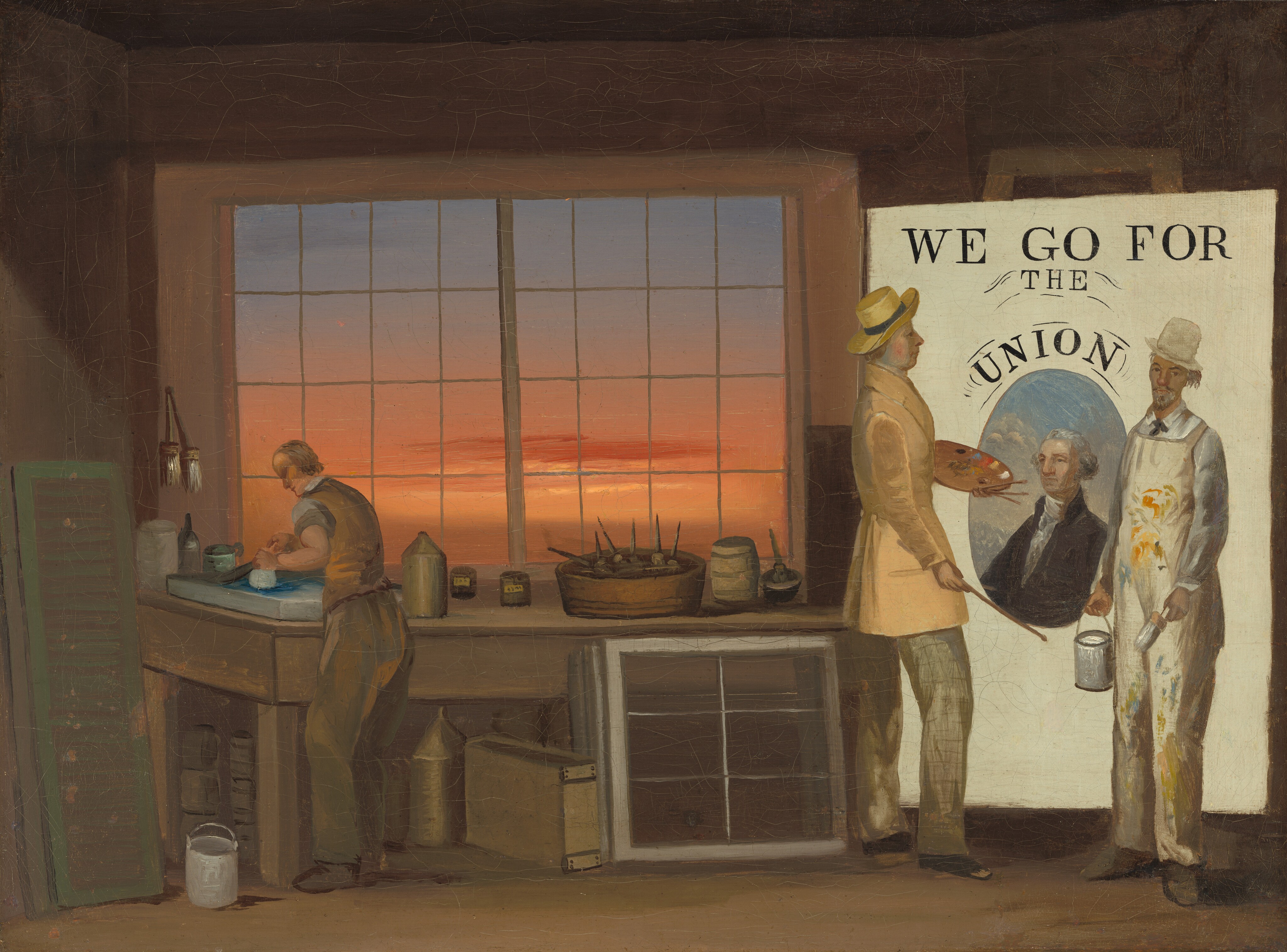 This painting depicts a workshop scene where a large political poster is being created. On the left, a man stands at a worktable surrounded by tools and materials, including paint cans, brushes, and containers scattered around. He wears a tan vest over a white shirt with the sleeves rolled up. On the right, two men stand next to a large white poster with the words "WE GO FOR THE UNION" above an oval portrait of a gray-haired man against a blue backdrop. The two men both seem to be painting the poster, with the man on the left holding a palette and a thin brush, and the man on the right holding a large can of white paint and a wide brush. The man on the left wears a tan coat and a yellow hat, while the man on the right has paint-covered overalls on over his white shirt and tie. The two men on the left have pale skin and clean-shaven faces, and we see them in profile. The man on the right looks out at us, and he has tan skin, a dark mustache, and a gray beard. In the center there is a window with a grid of rectangular panes, beyond which a vibrant orange and pink sky is visible.