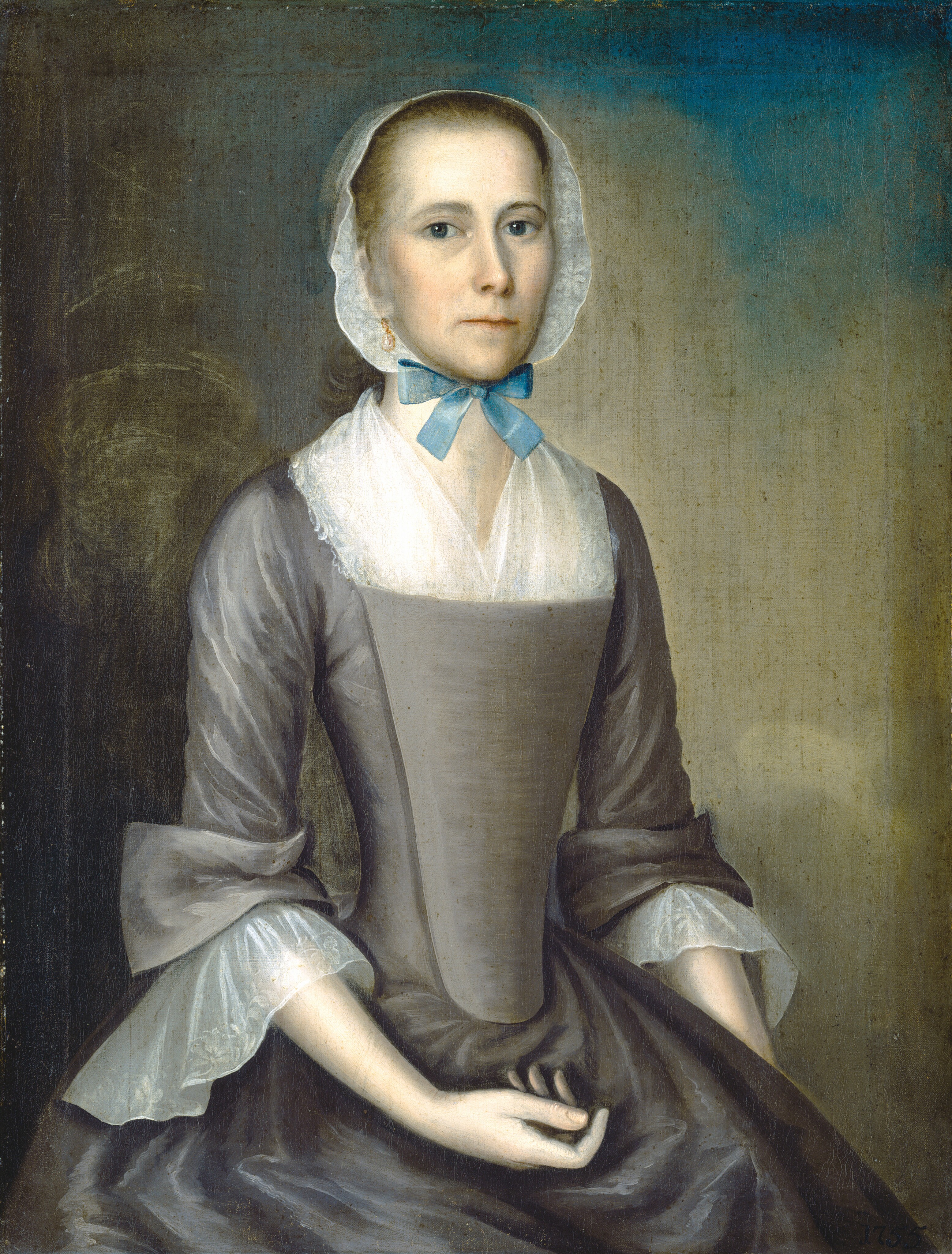 The image is a portrait showing the subject from the waist up. The person is seated with both hands resting on her lap. She has a neutral expression, light skin, blue eyes, and a modest hairstyle under a sheer white bonnet. She wears a formal dress in greyish-brown color with a fitted bodice, wide sleeves with white lace cuffs, a lace neckline, and a blue ribbon tied in a bow around her neck. The subject also wears small earrings. The background is a simple gradient of muted tones.