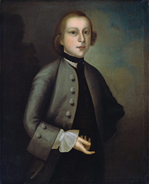 The image shows a young man with fair skin and a rounded face, wearing an 18th-century style outfit. He has light brown curly hair, a gray coat with large buttons, black collar, and white neckcloth. He stands with his right hand in his coat and his left hand slightly visible. The background is a combination of dark gray and light brown tones.