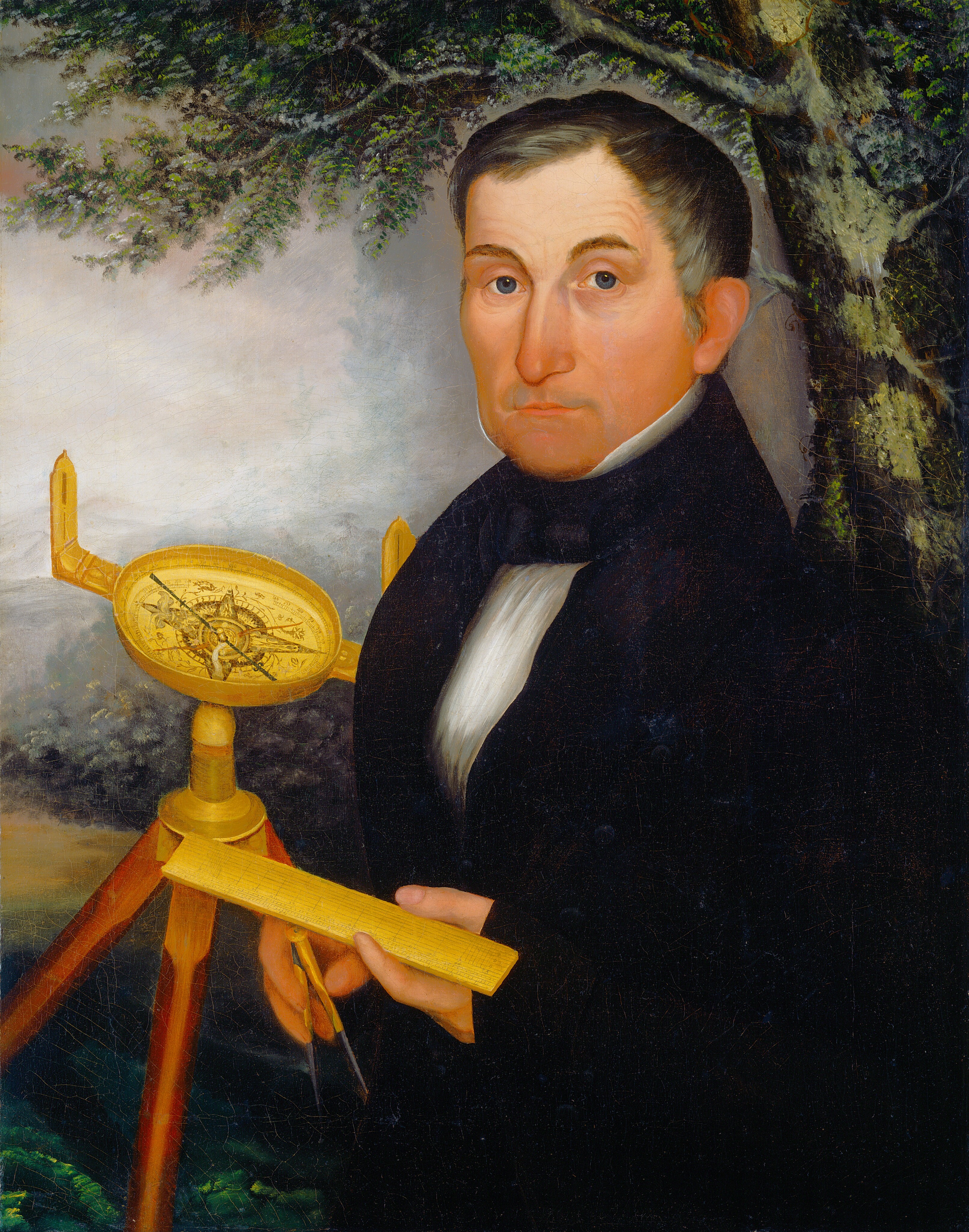 The image shows a man depicted from the waist up, holding surveying instruments in his hands. He is positioned facing slightly to the left while looking directly at the viewer. His facial features are distinct with a straight nose, thin lips, and light complexion, and his hair is short and dark, neatly combed back. He is dressed in formal attire consisting of a black suit with a white shirt and a black necktie. The man is holding a yellow ruler-like tool in one hand while the other hand holds a compass. Behind him, there is a surveyor's transit on a tripod. The background includes a tree with lush green leaves and a partially cloudy sky.
