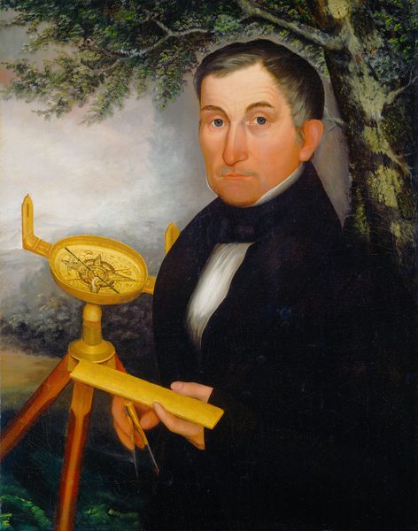 The image shows a man depicted from the waist up, holding surveying instruments in his hands. He is positioned facing slightly to the left while looking directly at the viewer. His facial features are distinct with a straight nose, thin lips, and light complexion, and his hair is short and dark, neatly combed back. He is dressed in formal attire consisting of a black suit with a white shirt and a black necktie. The man is holding a yellow ruler-like tool in one hand while the other hand holds a compass. Behind him, there is a surveyor's transit on a tripod. The background includes a tree with lush green leaves and a partially cloudy sky.