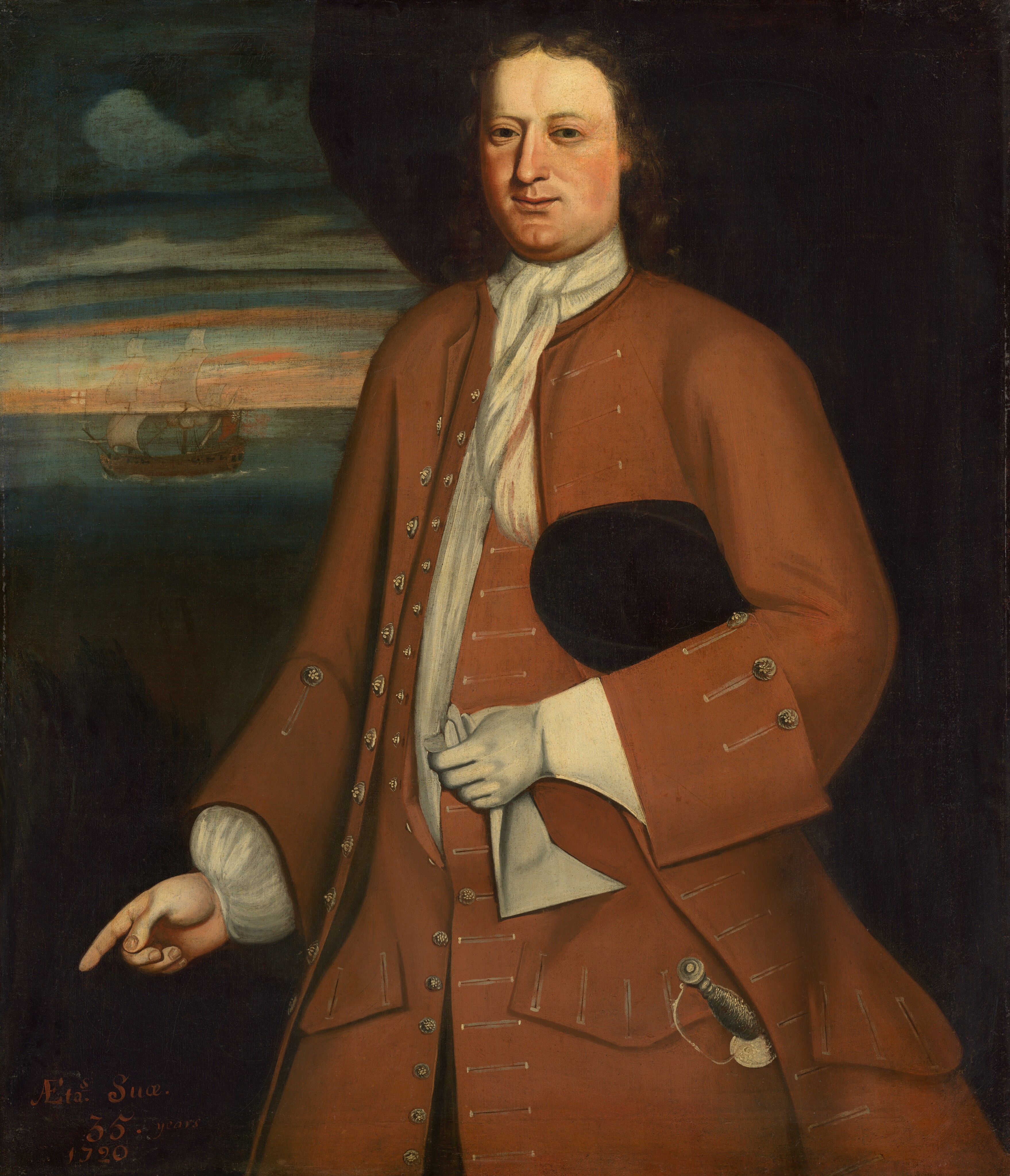 The painting depicts a man from the thighs up, standing and facing slightly to the left with his face turned towards us. His right hand appears to be pointing downwards towards the bottom-left corner. He has a broad face with fair skin, rosy cheeks, a long nose, and small eyes. His shoulder-length brown hair has a slight wave. The man wears a long rust-colored coat with silver buttons and a white cravat, along with a white shirt and cuffs at his wrists. His left hand wears a white glove, and he is holding the other glove in that hand. He also holds a black hat under his left arm and has a sword tied to his waist. The background is dark, with a cloudy sky visible on the left and a ship sailing on dark, calm waters.