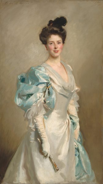 Shown from the knees up, a young woman with pale skin and flushed cheeks looks at us, wearing a long, shimmering white dress partially draped with powder-blue fabric in this vertical portrait painting. The brushstrokes are loose in her clothing but blended in her face, giving the portrait a soft, almost blurred look. Her body is angled to our right but she turns to look directly at us. Her dark, chestnut-brown hair is piled loosely on her head. A dark form could be a feather or small hat set to one side. Her eyes may be two different colors; her right eye is grayish-blue and her right eye looks almost green. She has a straight, snub nose, and her fuchsia-pink lips are parted in a small smile. There is a faint suggestion of a cleft in her pointed chin. Her white dress has a low, scooped neck and a tight-fitting bodice over a flaring skirt. Powder blue-fabric drapes over her right shoulder, closer to us, and might be pinned or pulled through a gold ring there. The blue fabric appears on her left hip, farther from us, suggesting it may wrap across her back. The sheen of the white dress and blue fabric suggests silk. The artist signed the work in cursive letters in the upper left, “John S. Sargent,” and dated it in the upper right, “1902.”