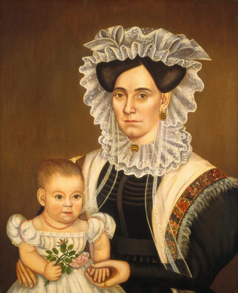 The image shows an upper body portrait of a woman and a child. The woman is seated and faces the viewer, with a serious expression. She wears a dark dress with a high neck and elaborate detailing, a shawl with ornate embroidery over her shoulders, gold earrings, and a brooch. Her hair is styled under a white laced cap. The child, with light hair, sits on the woman's lap, facing the viewer, wearing a white dress with lace details and a red bead necklace. The child holds a bouquet of flowers in one hand. The background is plain and dark.