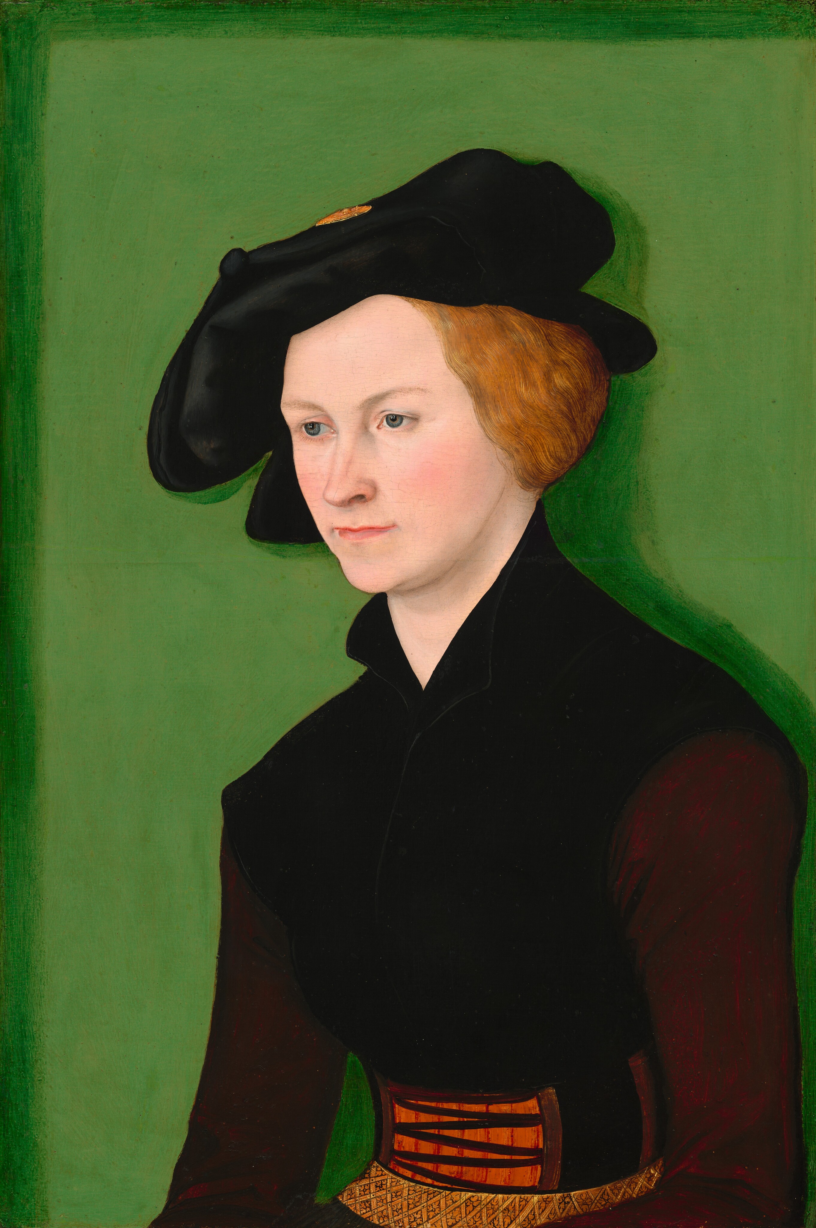 Shown from the lap up, a pale-skinned woman looks off to the left in front of a vivid green background in this vertical portrait painting. The woman’s whole body angles to the left as she gazes in that direction with gray eyes under faint brows. Her nose is indented on the long side, and her thin pink lips are closed in a line. Her strawberry-blond hair is pulled back over her left ear, to our right, and is otherwise hidden under a wide, floppy black cap. A glint of gold at the top of the hat could be her hair or a brooch or decoration. Her tightly fitting black bodice has a high collar. Her arms rest by her sides, and the sleeves are wine red. A belt around her narrow waist is laced with black on an orange band at the front, and a section below has a crosshatched pattern painted with delicate black lines on golden yellow. The woman is lit from our left and casts a darker green shadow on the lime-green background. The top and left edges of the panel are also lined with darker green.