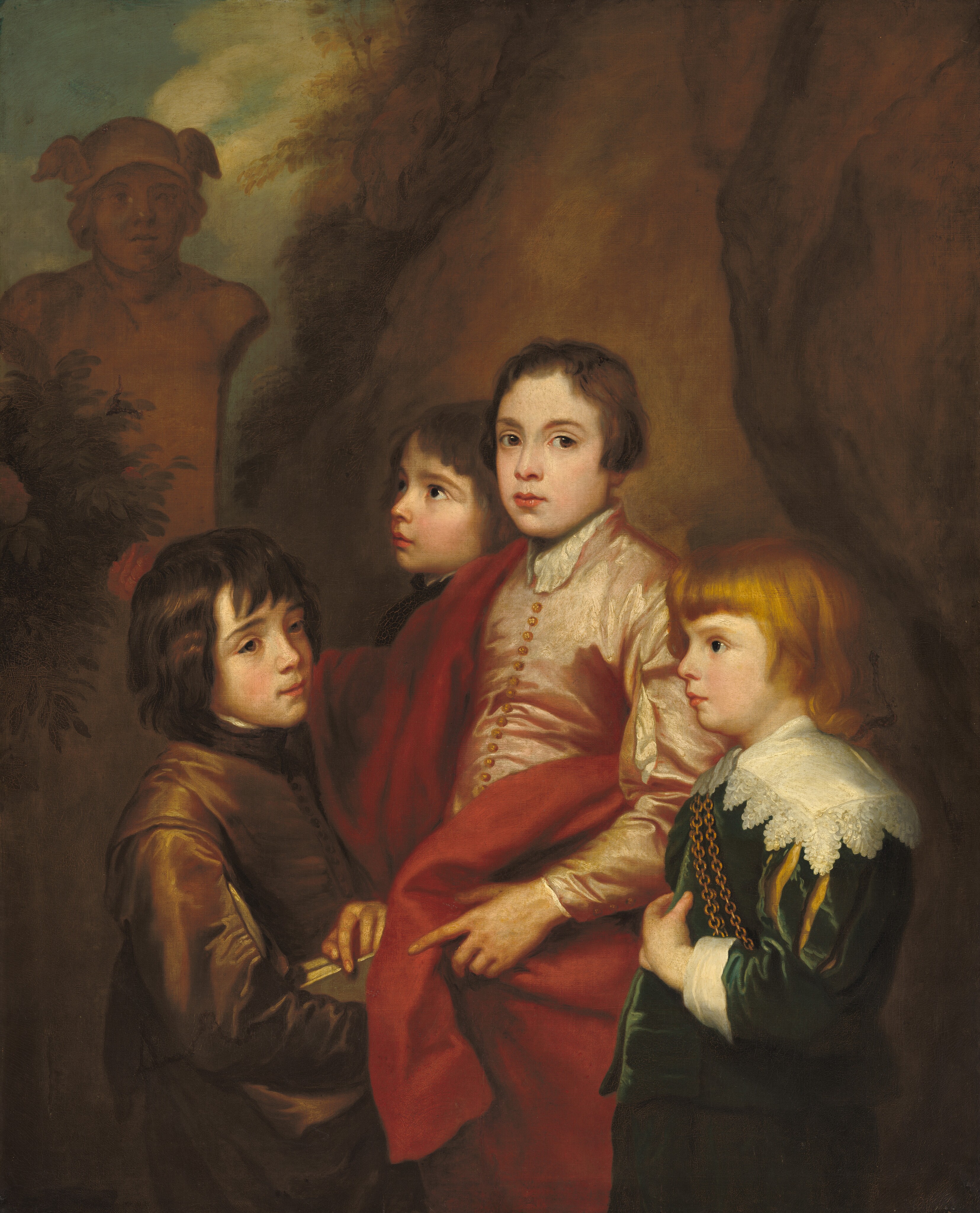 This painting shows four young boys with pale skin standing closely together. The central boy has wavy dark hair around his ears and is wearing a light pink garment with golden buttons and a red shawl over his shoulder. His head is turned towards us. To the right is a boy with shoulder-length reddish-blond hair, wearing a green coat with white lace shoulders and a gold chain. He is facing the left. On the left is a boy facing the right with dark, shaggy, shoulder-length hair, wearing a brown tunic with a high collar and holding a gray book or stack of papers. Partially visible behind the central boy is another boy in dark clothing on the left, facing left. In the background is a brown, rocky hill with a sculptural bust peeking through from dark green foliage on the left. There is a hint of a blue sky near the top left corner with some wisps of white clouds.
