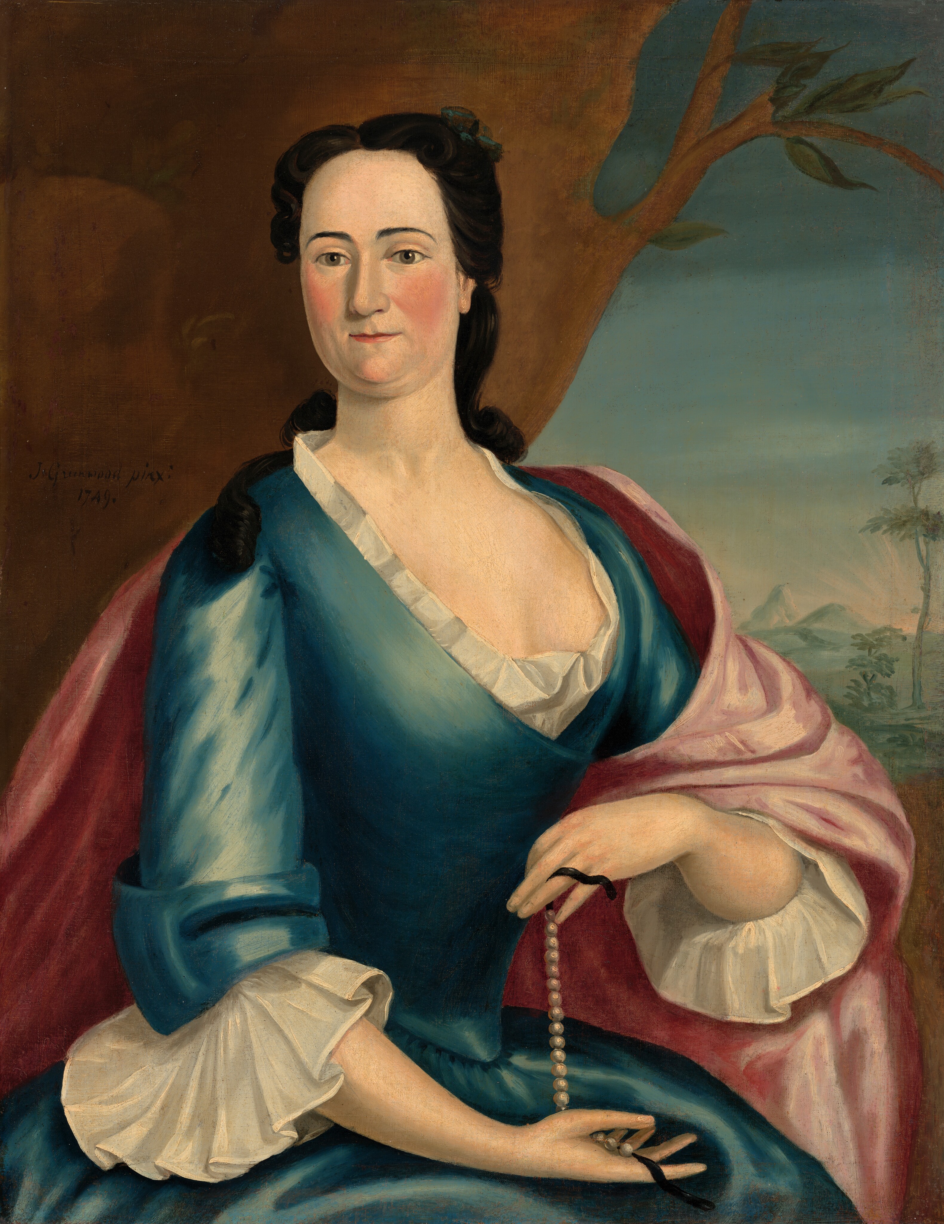 The portrait shows the upper body of a woman seated and turned slightly to her left, with her hands delicately holding a string of pearls. She has a composed facial expression with fair skin, rosy cheeks, dark eyes, and dark hair styled in tight curls, framing her face, and partially pinned up with a green decorative piece. She is wearing a deep blue dress with a low-cut neckline and white ruffled trim, accompanied by similarly styled ruffled cuffs on her sleeves. A pink drape is wrapped around her shoulders. In the background, there is a painted landscape depicting a tree with branches extending across the top part of the image on the left and a distant view of a sky transitioning to mountains and sparse foliage on the right.