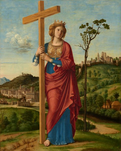 A pale-skinned woman stands holding a cross in front of a deep landscape in this vertical painting. The woman’s body faces us but she tips her head to our right and looks off in that direction with light brown, wide-set, large eyes. She has a long, straight nose, pale pink lips, and a square jawline. Her thick blond hair is pulled back and curls fall alongside her face and fall down to her shoulders. She wears a gold crown and gold breastplate ornamented with pearls and gems. Her lapis-blue gown is slit along the long sleeves and puffs of white linen are pulled through the openings. A carnation-red robe drapes over one shoulder and across her hips. She is barefoot, and both hands brace the tall cross to her right, our left. A tall, spindly tree with only a few leaves in its sparce canopy stands just behind her to our right. She stands on a grassy hill, and a path leads back to a town. More grassy, tree-lined hills behind her rise to another town outlined against the pale blue sky. A few clouds trundle across the sky and more are streaked across the pink horizon, which comes about halfway up this composition.
