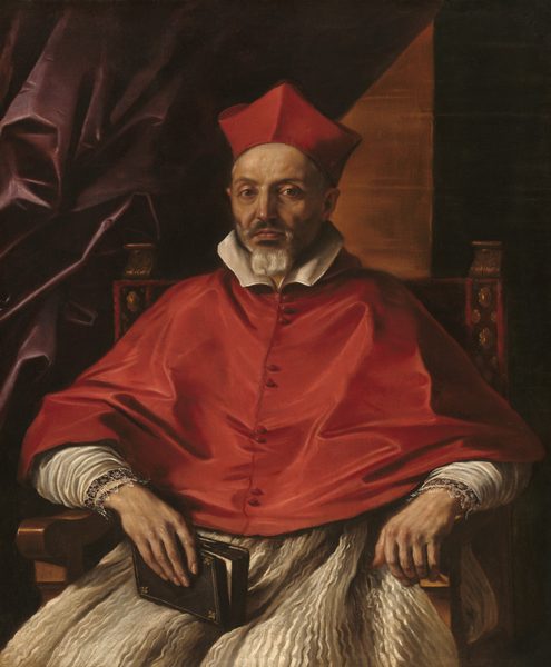 In this painting, a man is shown seated, facing forward, with a red biretta on his head. He has pale, wrinkled skin, deep-set eyes, a prominent nose, and a neatly trimmed grey beard and mustache. He wears a red garment over his shoulders and torso with a white collar and cuffs, and lace details on the sleeves, with a pleated white robe underneath. His forearms rest on the arms of the chair he sits in, and in one of his hands he holds a partially open book. The chair is ornately decorated, and the background shows dark purple drapery on the left and a dark wall on the right, with an illuminated triangle of lighter brown.