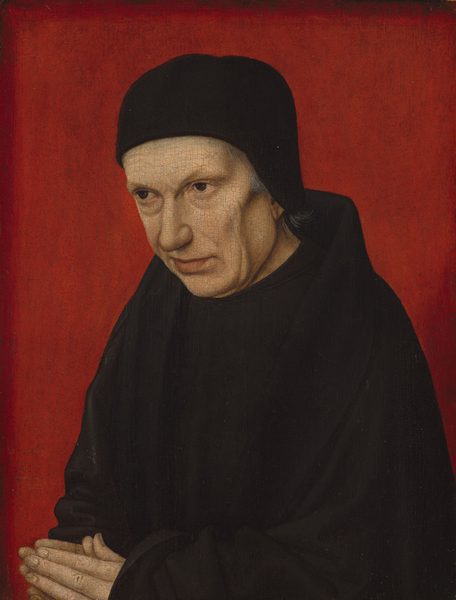 Shown from the waist up against a vivid red background, a pale-skinned, cleanshaven man looks off to our left in this vertical portrait painting. His body is angled to our left, and his head tilts down so he looks in that direction from under faint eyebrows. He has bags under brown eyes, sunken cheeks, and soft jowls. He has a rounded nose and wide chin. His pale pink lips are closed and the far corner appears to be pulled slightly back. A close-fitting brimless black cap nearly covers his gray hair, and he wears an inky-black cloak over a black robe. His hands are together in prayer in the lower left corner of the panel, and the background is scarlet red.