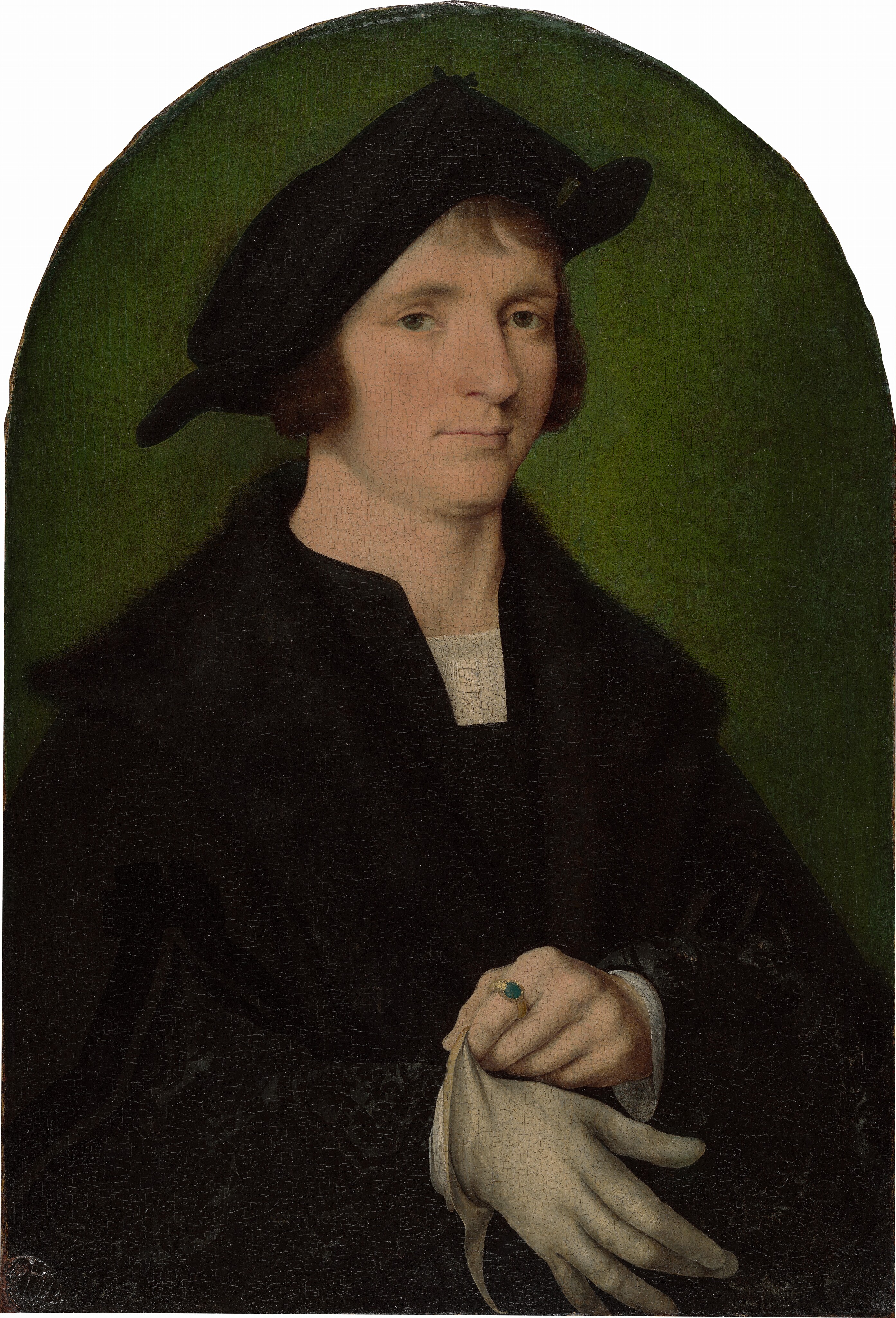 Shown from the waist up, a clean-shaven, pale-skinned man dressed in black gazes at us in this vertical portrait painting, which has an arched top. His body is angled to our right, but he glances back toward us with slightly drooping hazel-green eyes under slender brows. His face tapers to a narrow chin, and his pale pink lips are closed. His ear-length brown hair and bangs are mostly covered by a wide, black hat that sits cocked to our left. He wears a voluminous black coat with a wide fur collar over a black garment with a notched collar. A white shirt beneath is visible at the neck and cuffs. He pulls a bone-white glove onto one hand and wears a gold ring with a green gem on the index finger of his bare hand. The green background behind him glows around his shoulders and deepens to moss green around the arched top of the panel.