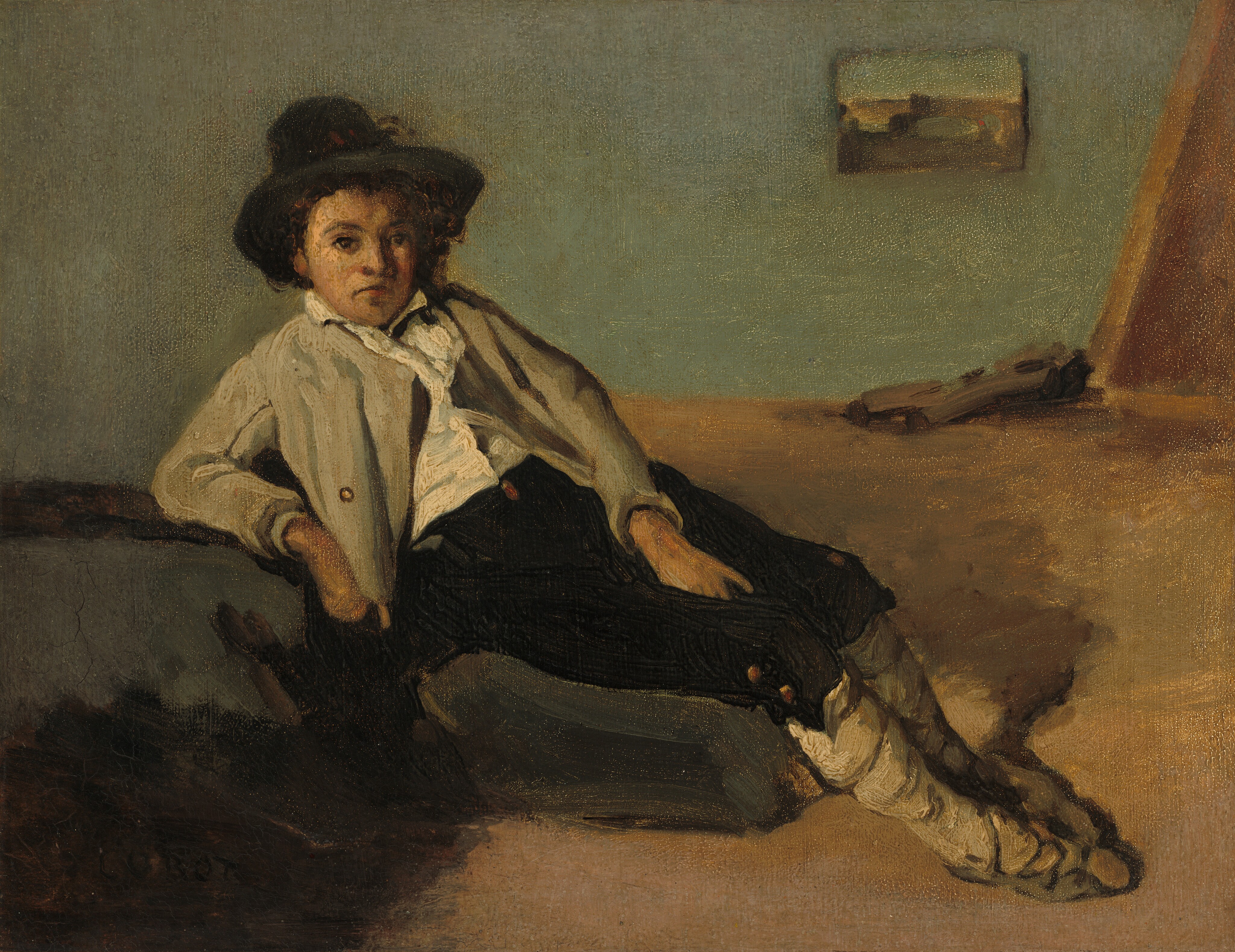 This painting depicts a young boy sitting in a relaxed position, with his right arm leaning on a black surface. He has pale skin, wide eyes, and a small, slightly downturned mouth. He is wearing a dark, wide-brimmed hat, a light-colored jacket over a white shirt, dark trousers, and what appear to be foot coverings made of wrapped cloth. The background shows a simple setting: a pale greenish wall, a framed piece of art or a window, and a block of wood on the floor in the corner of the image. The brushstrokes in the painting are visible, especially those in the floor and the boy's jacket.