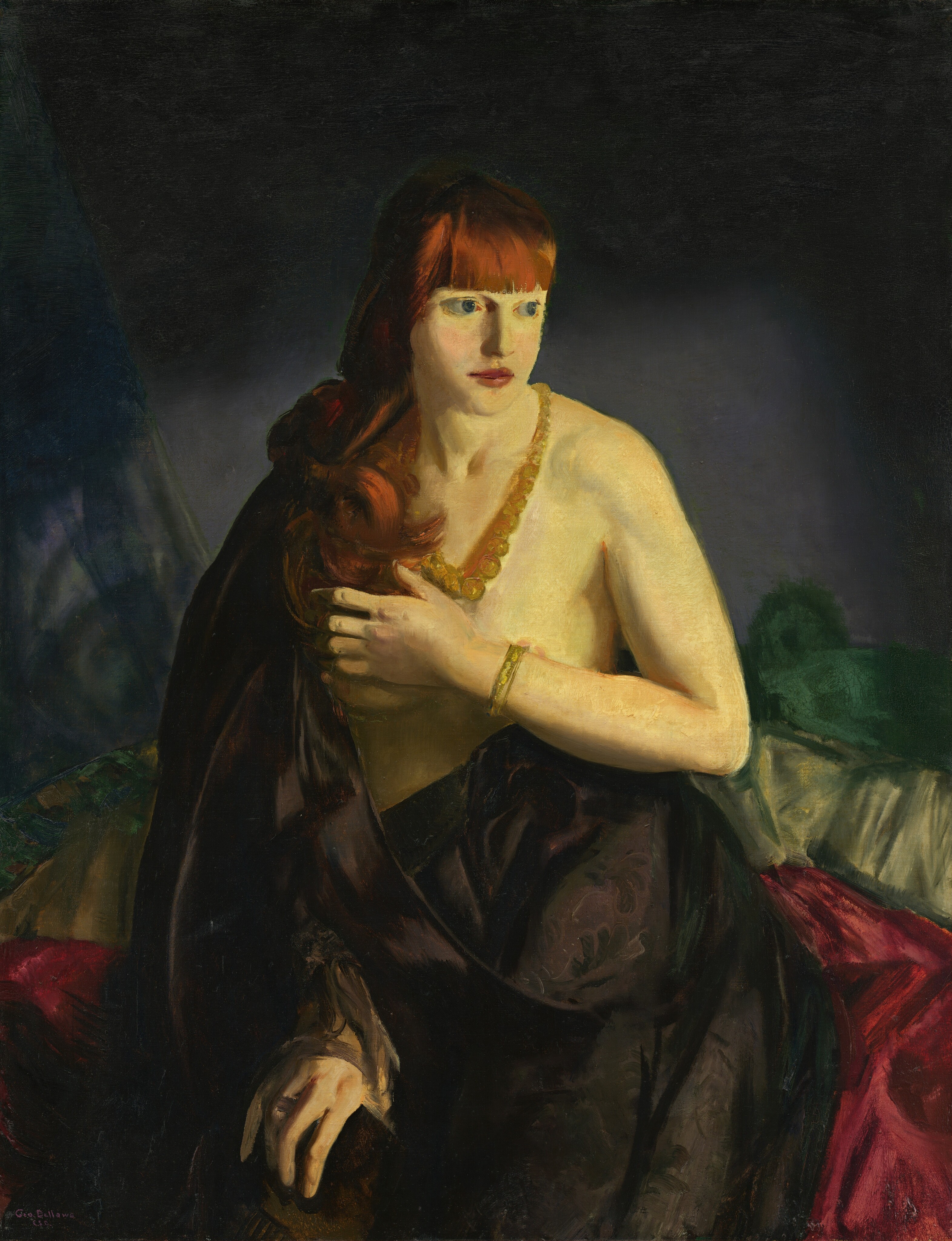 Shown from the knees up, a woman sits partially covered by a black cloth as she holds one forearm across her bare breasts in this vertical painting. The woman has pale, yellow-tinged skin and long, copper-red hair and bangs. Her body faces us, but she turns her head to look off to our right with large blue, wide-set eyes. Her cheeks are flushed, and her full, dark pink lips are closed. A strand of gradually larger amber-yellow beads hangs around her neck, and she wears a gold-colored bracelet on the arm braced across her chest, her left arm, to our right. Glimpses of pale pink nipples are visible. The voluminous black cloth drapes down over one shoulder and across her hips. She wears a ring on the other hand, which emerges from the cloth to rest on that knee. Piles of garnet red, peridot green, and forest green are piled up to chest height behind her, and the background is nickel gray around her body and darkens to black around the top and side edges. The scene is loosely painted, especially in the fabric and background. The artist signed the canvas in the lower left corner, “Geo. Bellows E.S.B.”