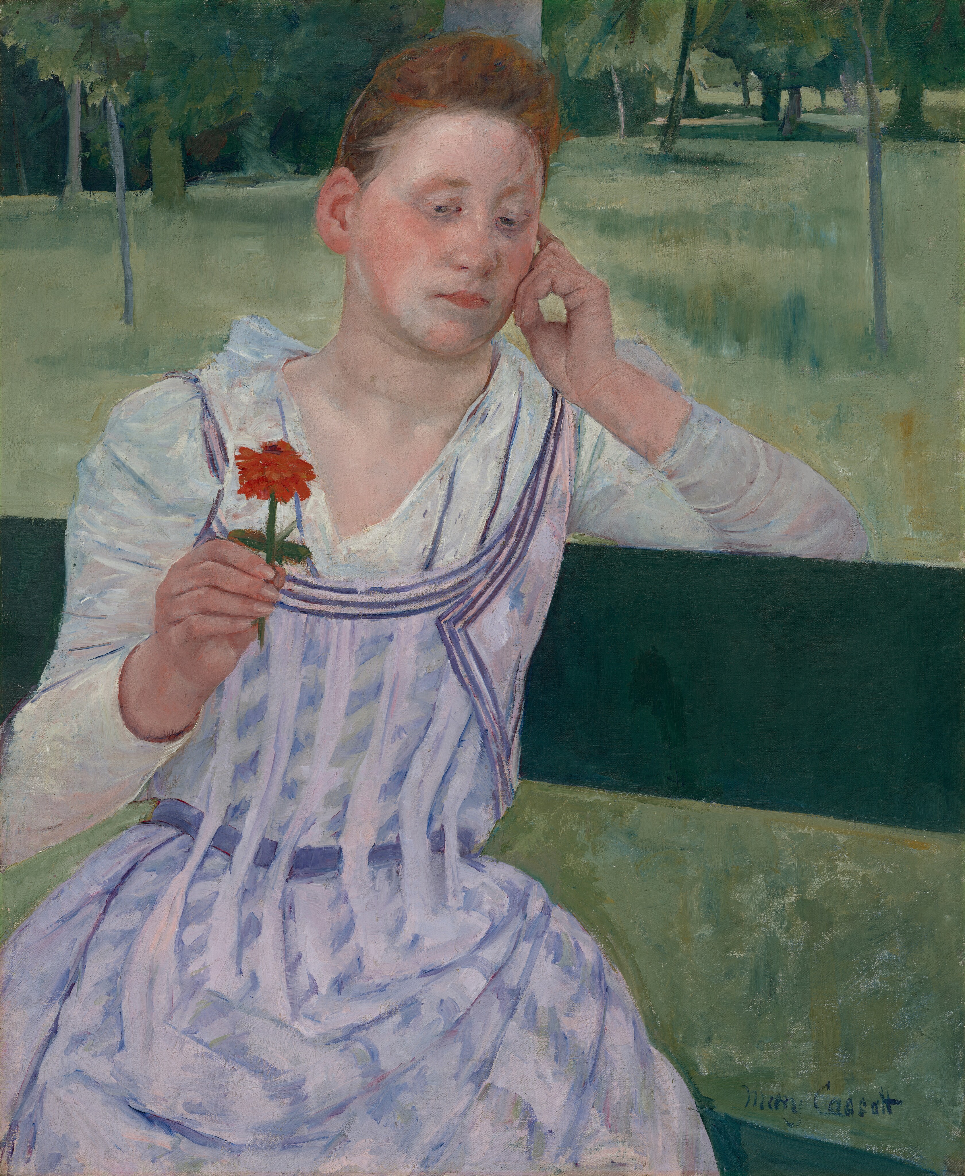 Shown from the knees up, a young woman with peachy skin and red hair sits facing us on a pine-green bench in this vertical painting. She sits with her body angled to our right, and her left elbow, on our right, hooks over the top slat of the bench. Her head tilts slightly to our right to rest on the curled fingers of that hand. In her other hand, she holds up a red flower on a short stem. Her hair is pulled up and back over a high forehead, and her cheeks are deeply flushed. Her pink lips are closed, and she looks down and to our left at the flower with gray eyes. She has an oval-shaped face and a hint of a double chin. Her white dress is painted with ice-blue shadows and folds. It has a deep V neck that reaches to an apron-like pinafore patterned with vertical bands of pale lilac that alternate with angled daubs of blue. Beyond her is a loosely painted landscape with grassy areas and clusters of tall trees painted in spring, emerald, and sea glass green. The edge of the grassy field nearly brushes the top edge of the canvas, and the trees are cropped by it. The artist signed the lower right, “Mary Cassatt.”