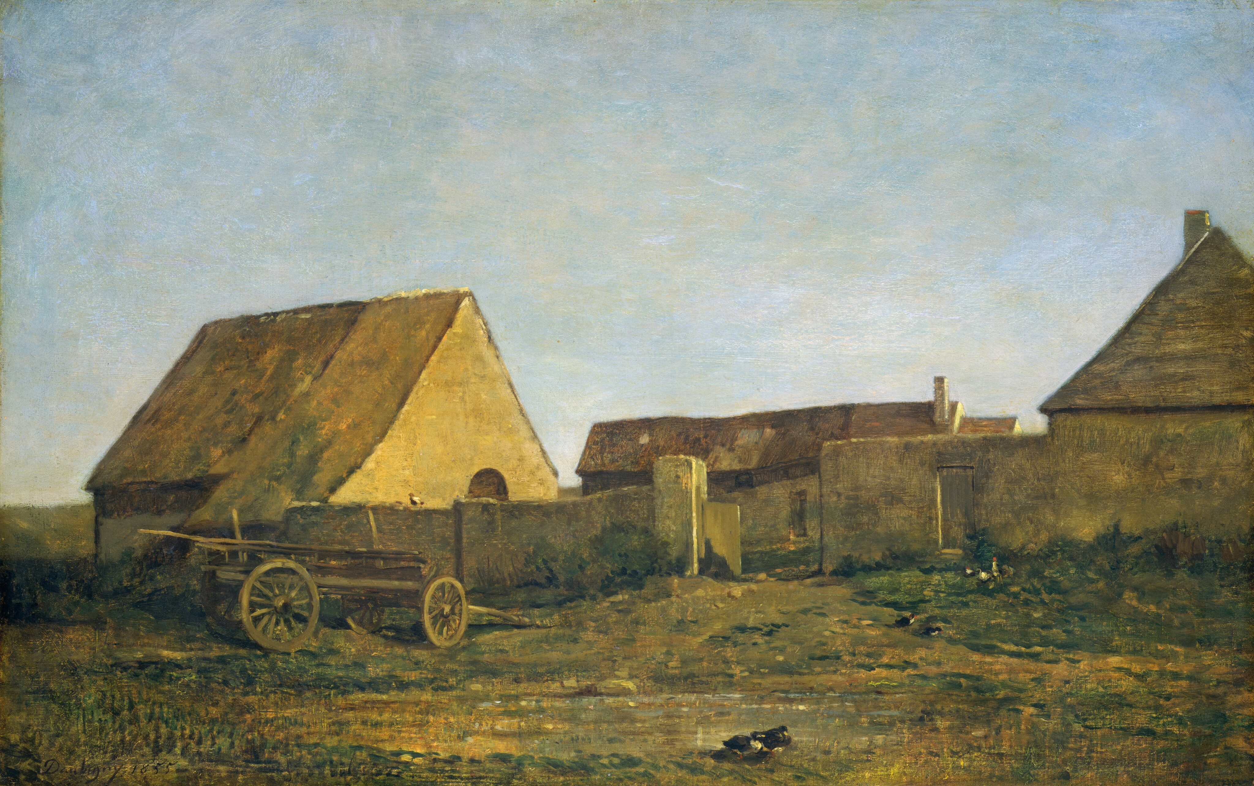 This painting depicts buildings under a clear blue sky. The horizon line is low, mostly obscured by the structures. The buildings have pointed brown roofs, and they are a pale yellow color. They are surrounded by a low yellow-gray stone wall. In front of the wall is an area of grass and dirt with a wooden wagon with two large wheels on the left and small black and white birds pecking at the ground on the right. The scene appears to be illuminated by golden light. The brushstrokes in the painting are visible, especially in the sky and buildings.
