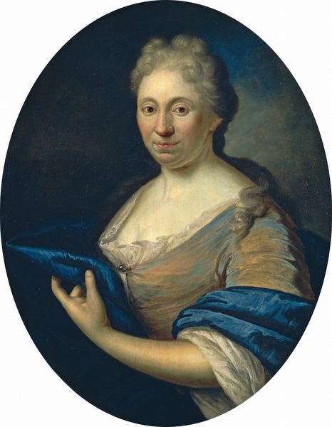 The image shows a woman from the waist up. She is turned slightly to her right, looking straight at the viewer. She has fair skin, round cheeks, and a gentle gaze. Her hair is styled back in soft curls or waves. She is wearing a garment with a pale bodice and a layer of rich blue fabric wrapped around her shoulders. Her right hand is raised, holding the edge of the blue fabric. The background is a smooth, dark, neutral gradient.