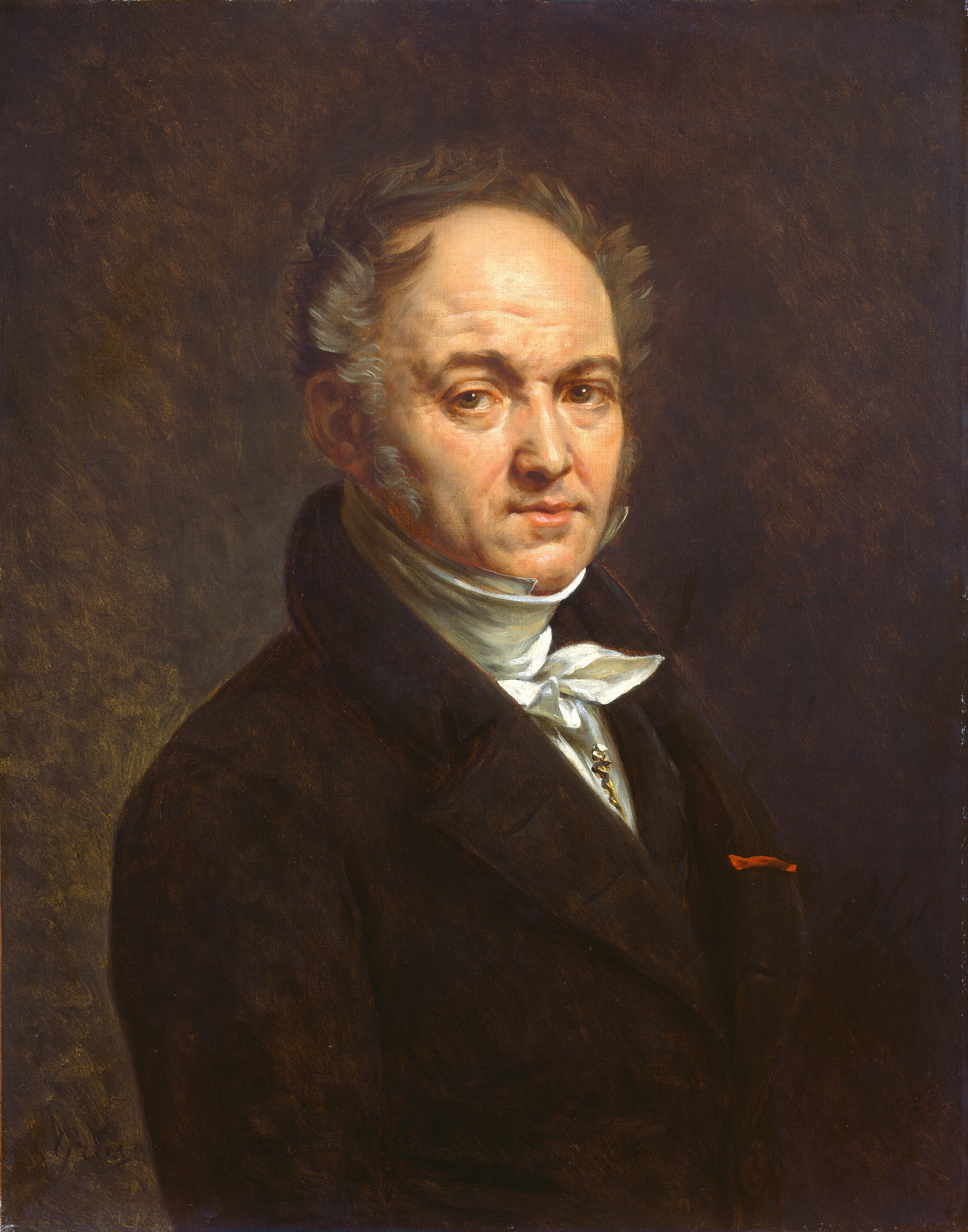 The image shows a man from the waist up. He is slightly turned to the side, with a serene expression. He has short, swept-back gray hair, sideburns, and visible lines on his face. The man is wearing a dark suit, white high-collared shirt, and a white cravat. A chain, possibly a watch fob, is visible on his suit. There is a red detail, possibly a ribbon or handkerchief, in his breast pocket. The background is plain dark brown.