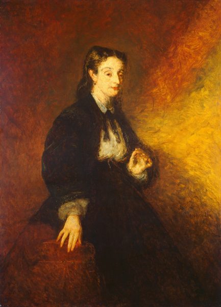The image shows a woman seated in a three-quarter view, with her right hand on a surface and her left hand near her chest. She has a calm facial expression, fair complexion, dark eyebrows, light-colored eyes, and dark wavy hair falling past her shoulders. The woman is dressed in a dark, high-collared garment with a white blouse underneath and a bow at the neck. She wears a hoop earring in her left ear. The background consists of warm brown and yellow tones.