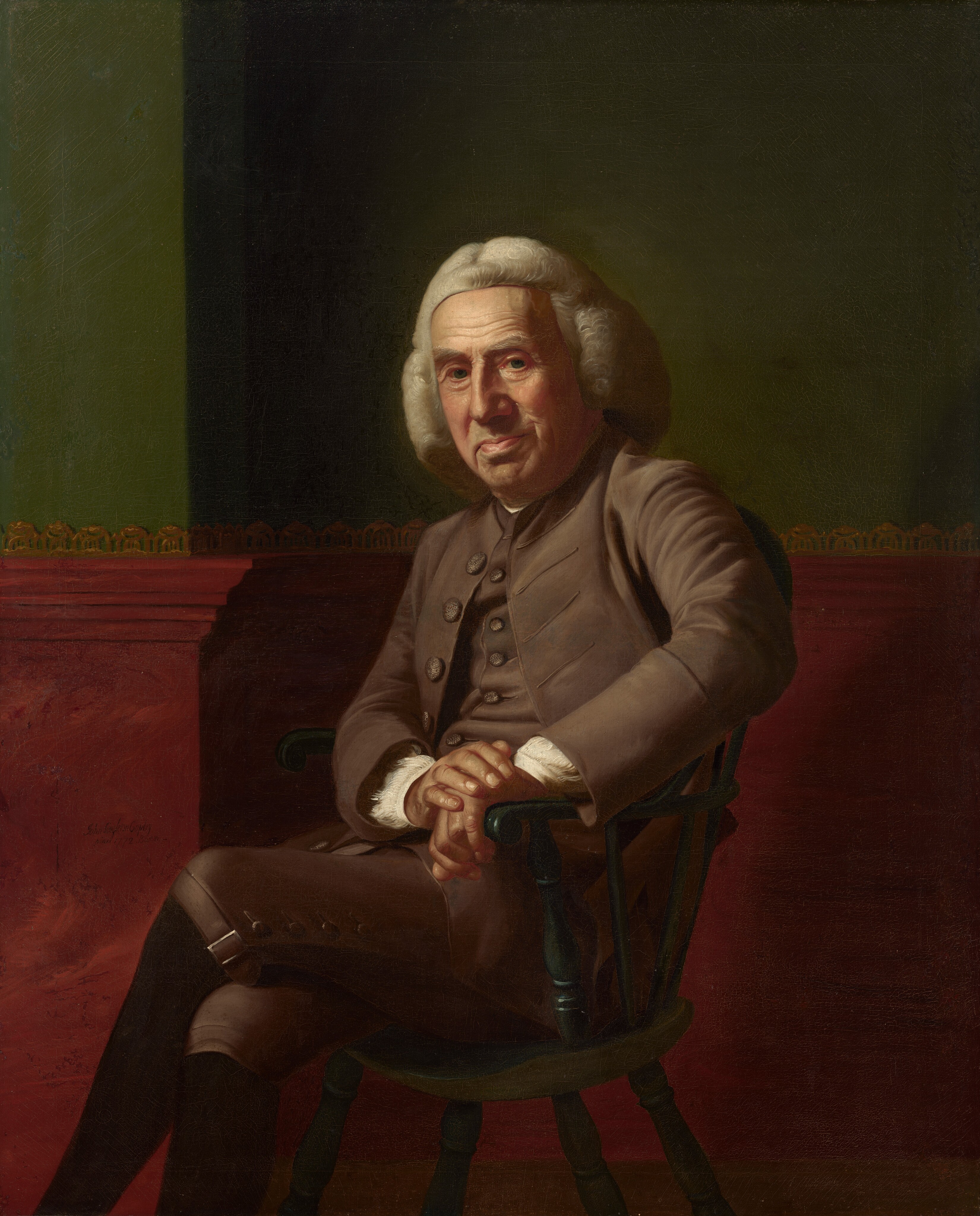 A pale-skinned, clean-shaven man with a heavily lined, paunchy face sits against a green and red wall in this vertical portrait painting. The man sits in a wooden chair painted forest green and rests both hands on the closer arm. His body and knees are angled to our left, and he turns his wide, square face to look at with heavy-lidded eyes. One brow seems slightly cocked, and he has a large nose. His lips are pulled up on one side over a round double chin. He wears a white, shoulder-length wig and a sable-brown suit. The cuffs of a white shirt are visible at his wrists where his hands are stacked on the arm of the chair. The knee-length breeches are buckled at the knee over black stockings. His legs are crossed away from us, and his feet extend off the bottom edge of the composition. The bottom half of the wall behind him is painted burgundy red up to and including a chair rail, and the wall above is moss green. The wall is lined with a gold scallop pattern along the top of the chair rail and a sliver of brown on across the bottom of the composition suggests a wood floor. The artist signed and dated the painting as if he had inscribed the red wall near the man’s knees, “John Singleton Copley pinx 1772. Boston.”