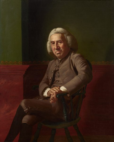 A pale-skinned, clean-shaven man with a heavily lined, paunchy face sits against a green and red wall in this vertical portrait painting. The man sits in a wooden chair painted forest green and rests both hands on the closer arm. His body and knees are angled to our left, and he turns his wide, square face to look at with heavy-lidded eyes. One brow seems slightly cocked, and he has a large nose. His lips are pulled up on one side over a round double chin. He wears a white, shoulder-length wig and a sable-brown suit. The cuffs of a white shirt are visible at his wrists where his hands are stacked on the arm of the chair. The knee-length breeches are buckled at the knee over black stockings. His legs are crossed away from us, and his feet extend off the bottom edge of the composition. The bottom half of the wall behind him is painted burgundy red up to and including a chair rail, and the wall above is moss green. The wall is lined with a gold scallop pattern along the top of the chair rail and a sliver of brown on across the bottom of the composition suggests a wood floor. The artist signed and dated the painting as if he had inscribed the red wall near the man’s knees, “John Singleton Copley pinx 1772. Boston.”