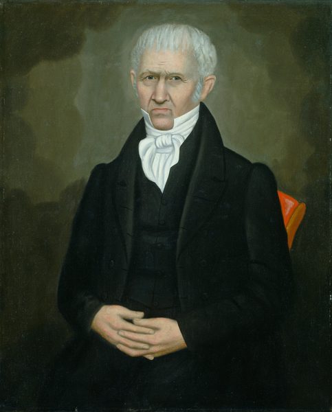 The portrait shows the upper half of a man seated with his hands clasped in front. The man has a slightly stern expression with deep-set eyes and light, bushy eyebrows. He has short, white, neatly combed hair. He wears formal clothing including a black coat, buttoned vest, high-collared white shirt, and intricate cravat. The background is a dark, uniformly painted surface. A chair with a bit of red fabric is partially visible, adding contrast to the dark backdrop.