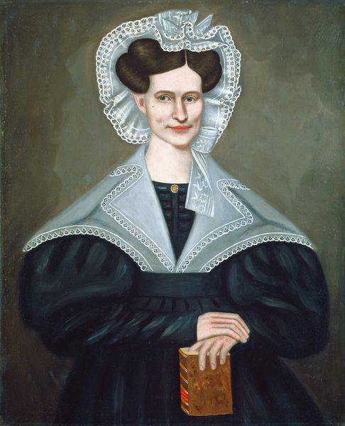 The image depicts a woman from the waist up. She is facing forward with her hands resting on a book held upright. She has a composed expression with light skin, defined lips, and prominent cheekbones. Her hair is styled in a neat updo, and she wears a lace-trimmed bonnet. She is dressed in a dark, full-sleeved dress with a lace collar and a pin at the center. The background is a muted brown.