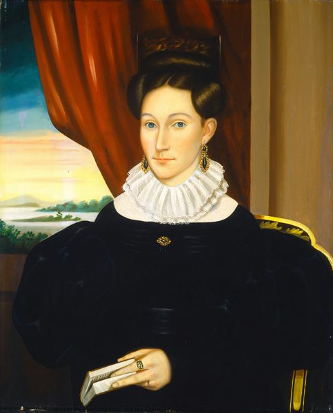 The image shows a half-length portrait of a woman seated in a chair. She is facing slightly to her right, with her gaze directed towards the viewer. She has fair skin, blue eyes, and a solemn expression. Her hair is dark brown and styled in an elaborate updo with large, smooth rolls on either side of her head. She wears a black dress with voluminous sleeves and a high white ruffled collar. She has a brooch around her neck, gold earrings, and a ring with a green stone on her left hand, which is holding a book. The setting features a dark red curtain behind her, partially pulled back to reveal a countryside landscape through a window. A portion of the chair with a curved golden edge is also visible to her left.