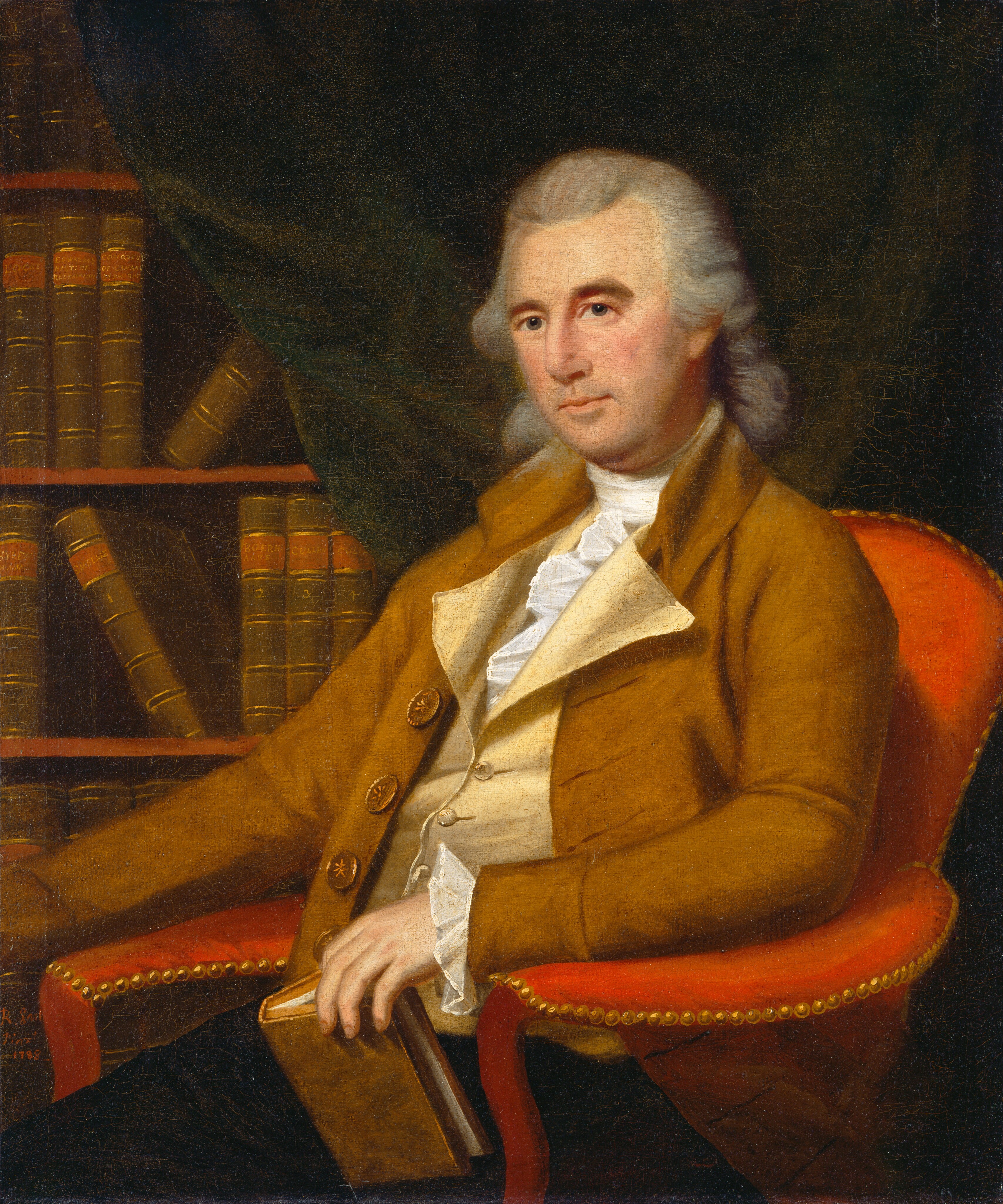 The image shows an upper-body portrait of a seated man. He is positioned in an angled chair, facing slightly to his right. His facial features include a composed expression, a narrow nose, and focused eyes, with a prominent forehead framed by his powdered, shoulder-length hair. The man is dressed in a brown coat with large buttons over a pale waistcoat and a white, ruffled shirt. He holds a book in his left hand, resting it on the arm of the chair. The chair is upholstered in red fabric with a gold-studded trim. In the background, there is a bookcase filled with books, partially visible. The dark drapery provides contrast and depth to the setting.
