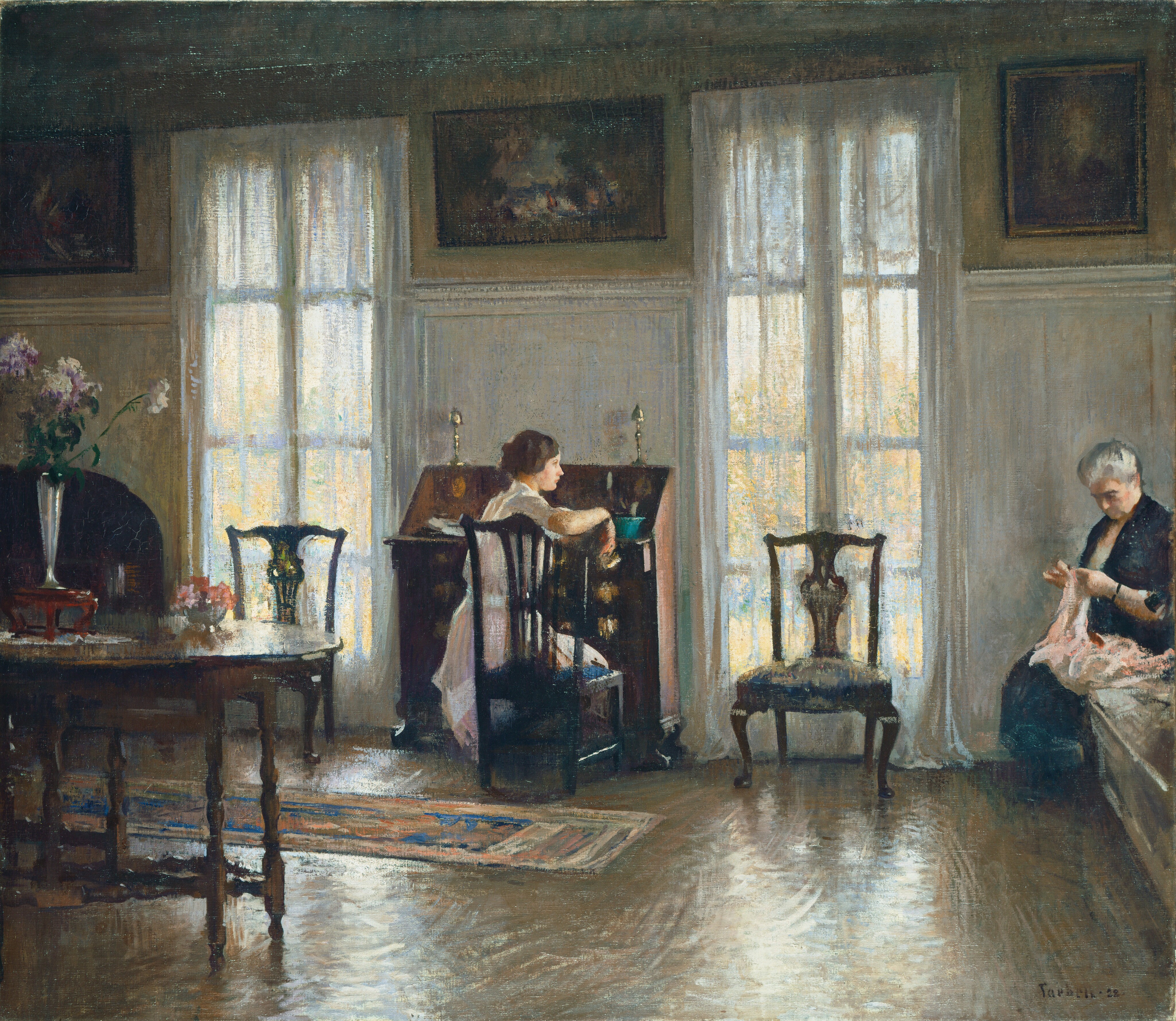 This painting shows two women in a room. At the center of the painting, a young woman is seated at a desk, her hand resting on the back of the chair, opening a small drawer. Her back is to us, but her head is turned to the right, allowing us to see her in profile. She has pale skin and brown hair in an updo behind her head, and she wears a light pink dress with white details around the waist and neck. On the right, an older woman is seated on a bench, engaged in an activity with her hands, perhaps knitting or sewing with strands of pink fabric or yarn. She has pale skin and gray hair pulled back from her face, and she wears a dark blue dress. The room around the women is elegantly furnished, with a wooden table on the left, more wooden chairs, large windows with curtains on either side of the desk, and paintings along the top edge of the yellow wall. The floor is brown and polished, reflecting white and yellow light from the large windows. The brushstrokes in the painting are soft and visible.