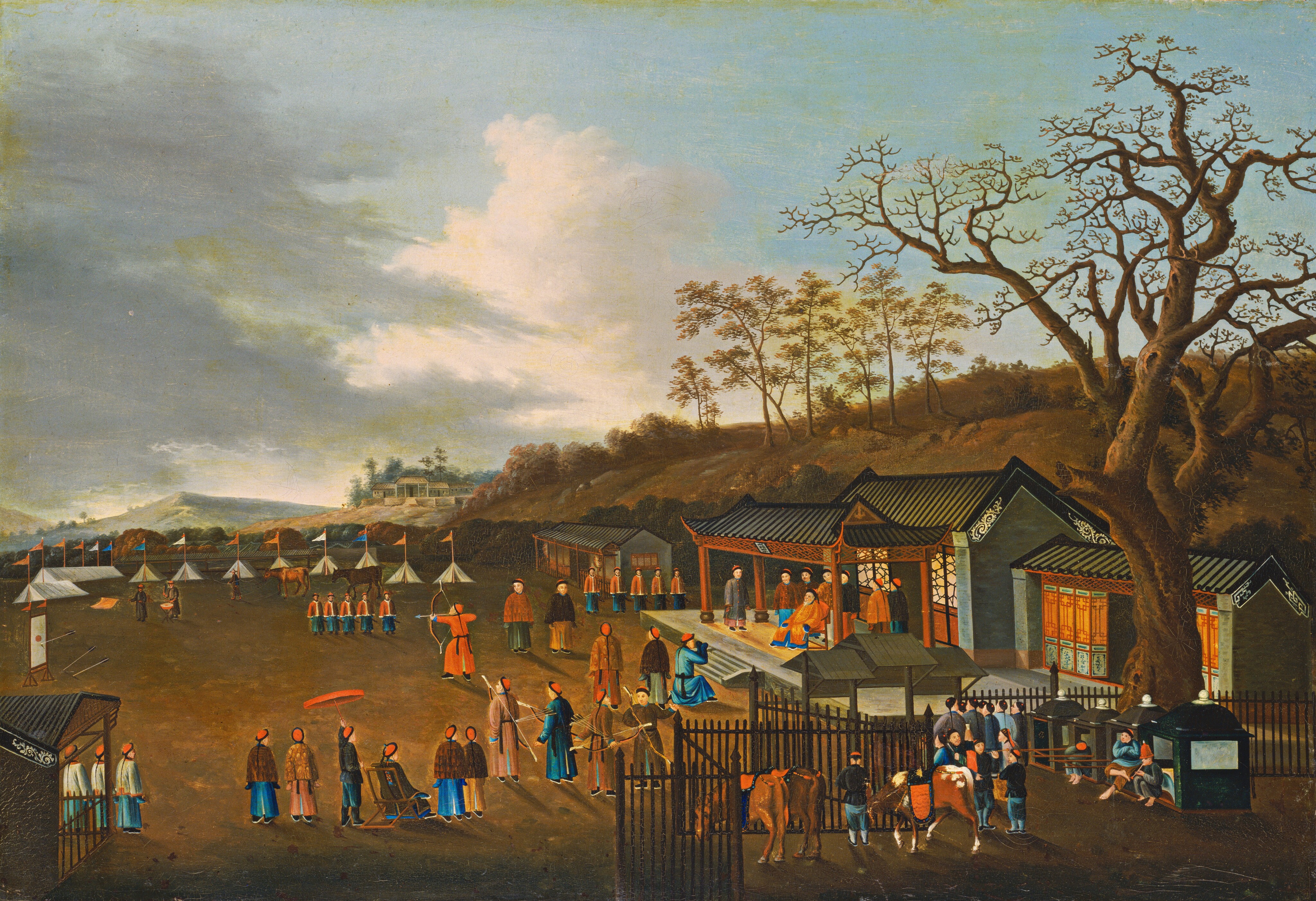 The painting features a busy scene with various activities taking place outdoors under a wide, open sky. Closest to us, on the right, there are people in long blue and gray garments standing next to several horses tied to a fence near a tall brown tree. In the center, a group of people are participating in an archery demonstration or competition, with targets set up on the left side. A group of people holding bows and arrows watch a person in the center wearing a long red outfit aim a bow at the target. The area is filled with numerous people, some walking, others watching. To the right, behind the fence with the horses, is an ornate building with gray walls and a black roof where another group of people is seated under a carved wooden canopy. At the center of this group is a person in long orange robes who sits facing the archery contest. A person in blue on the left kneels down towards this seated person. All the people in the painting have light skin and dark hair in long braids down their back, and they wear red hats. In the distance are several white tents flying flags of different colors. Behind them, the landscape is full of green and rusty-orange trees, with green and tan hills rising up below a wide blue sky full of white-and-gray clouds.